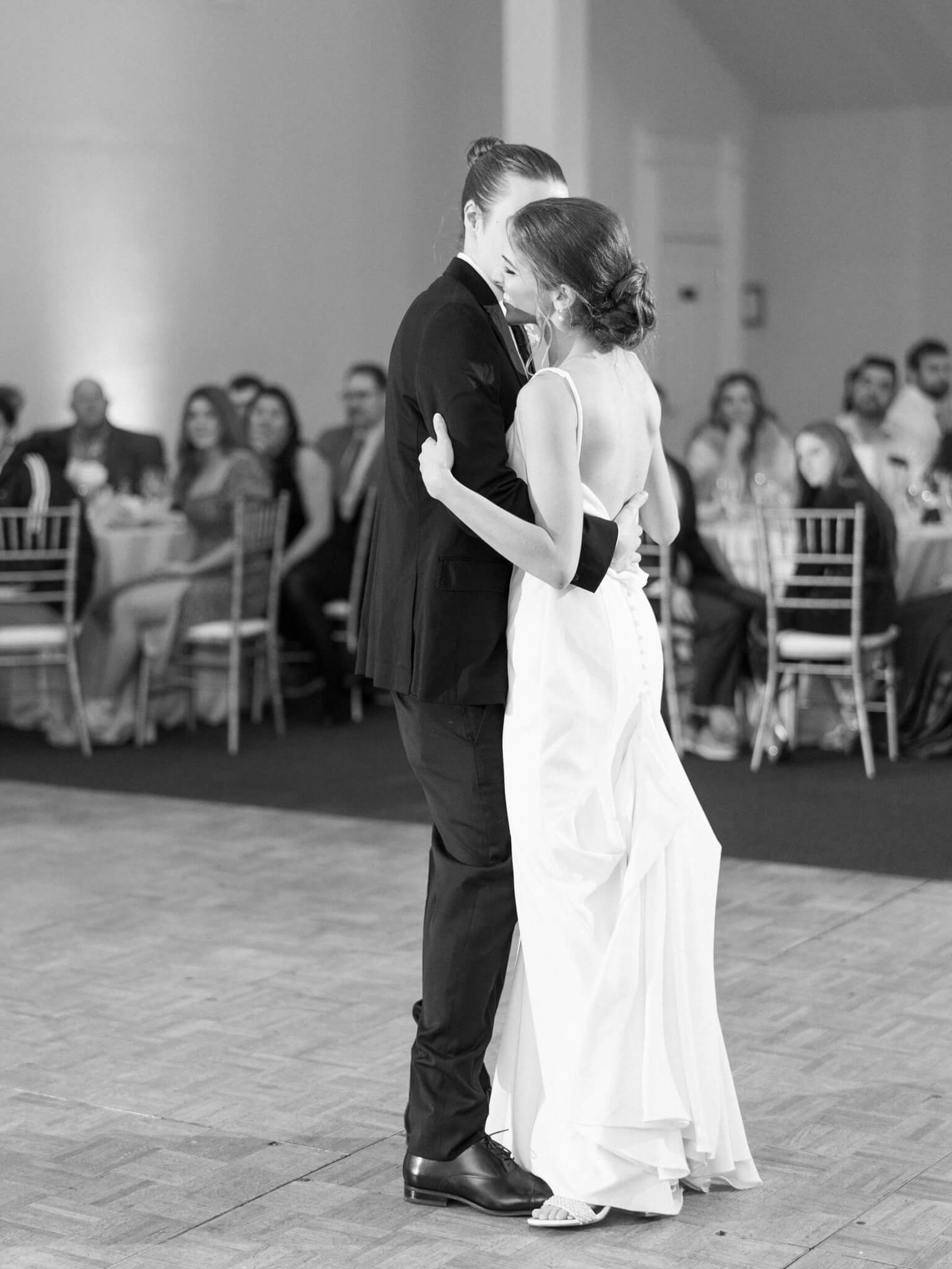Full length black and white of a bride and groom during their first dance with their guests in the background at Springfield Manor.