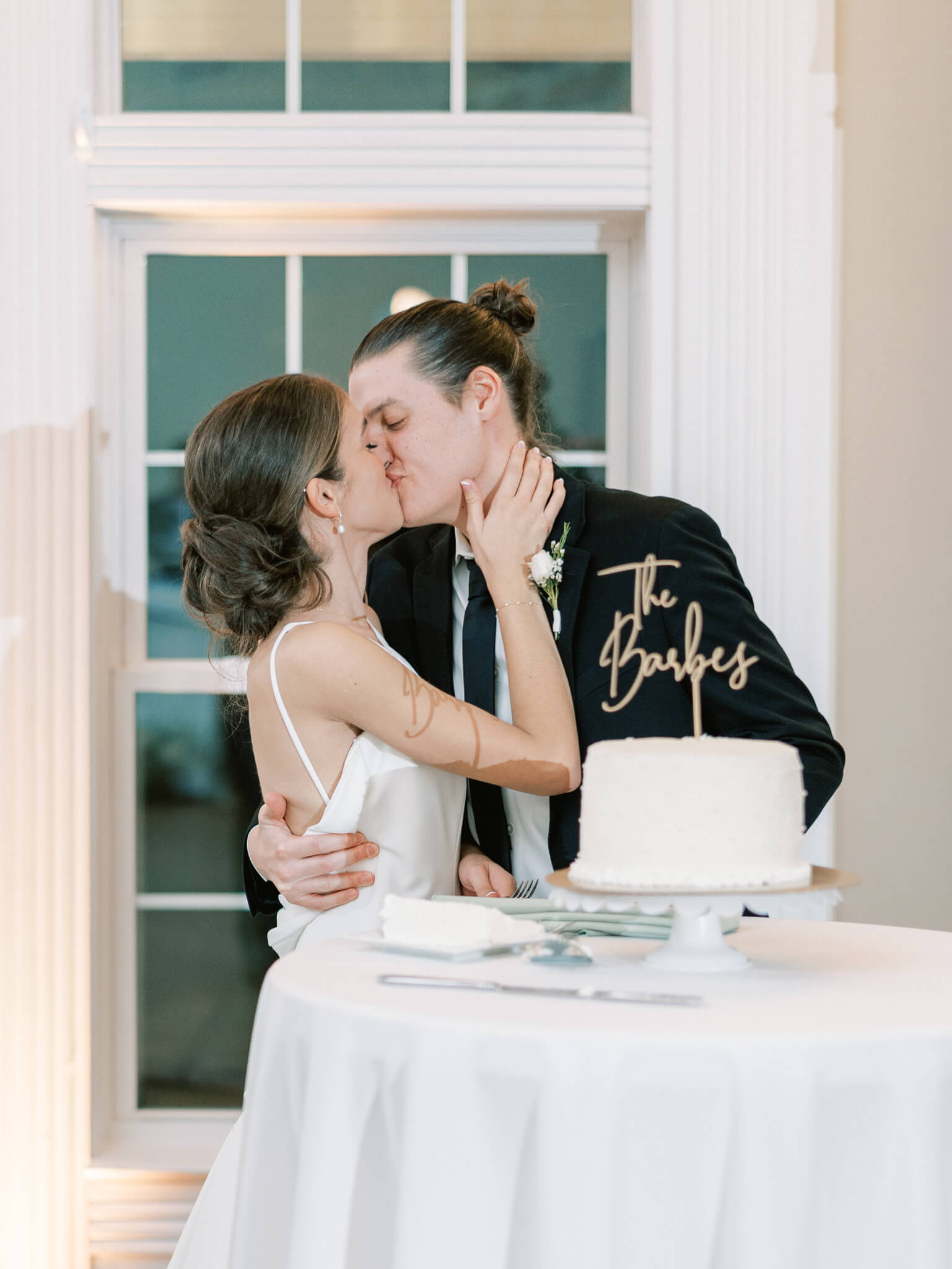 Close-up of a bride and groom kissing after cutting their white one tier wedding cake.