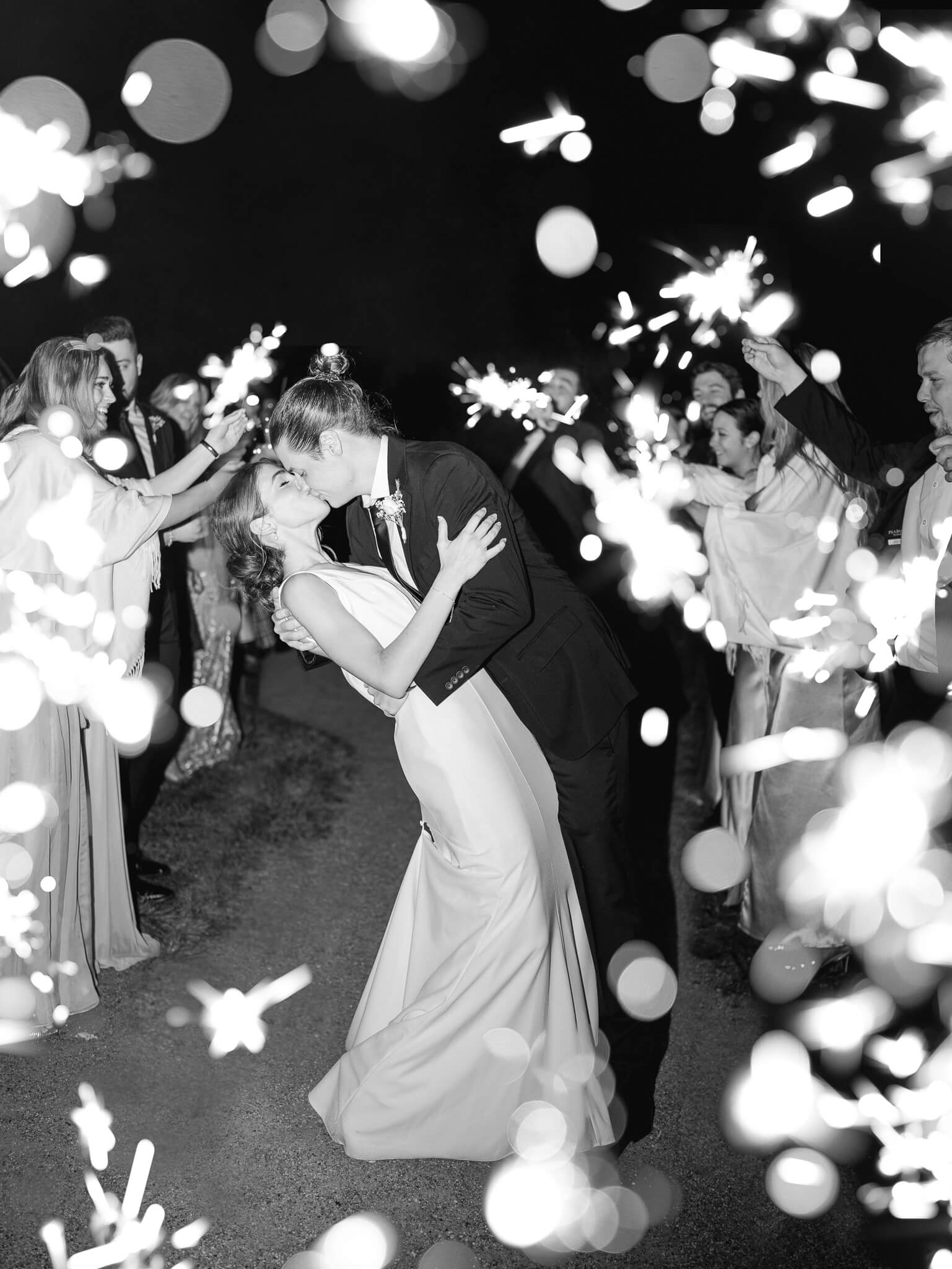 A black and white of a groom dipping and kissing his bride during the sparkler exit.
