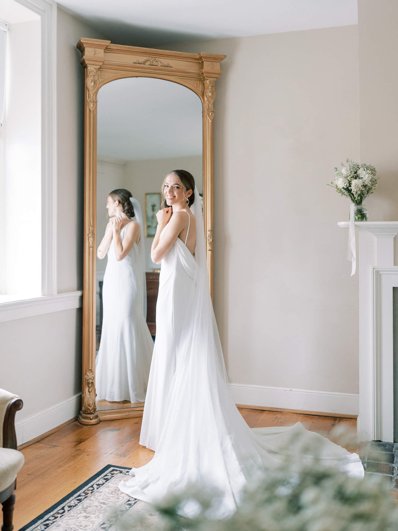 A bride in her wedding gown in front of a mirror, looking back over her shoulder.