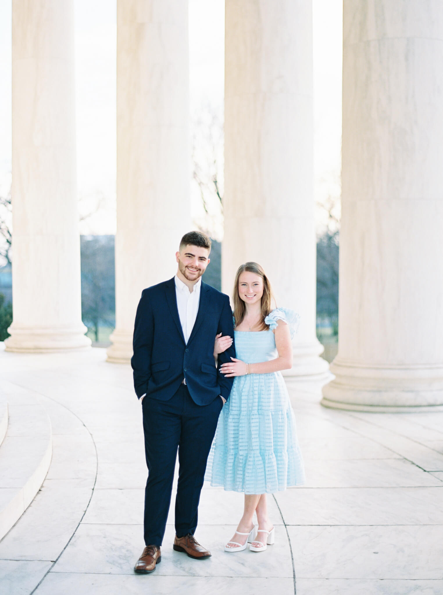 A young man and woman wearing formal attire standing in front of the marble columns during their Jefferson Memorial Engagement Photos