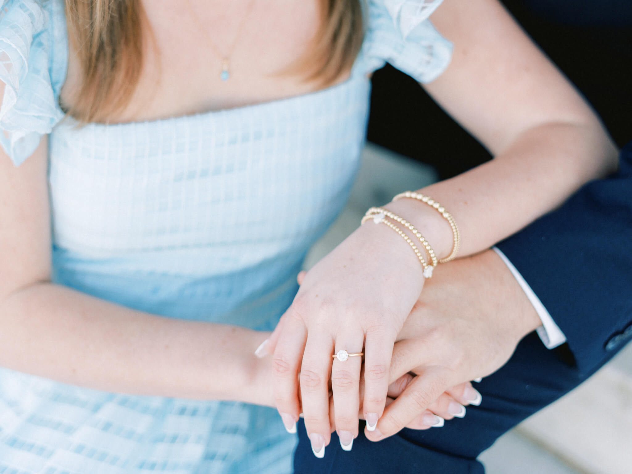 Close up of a woman's hands over a man's hands showing off her gold and diamond engagement ring.