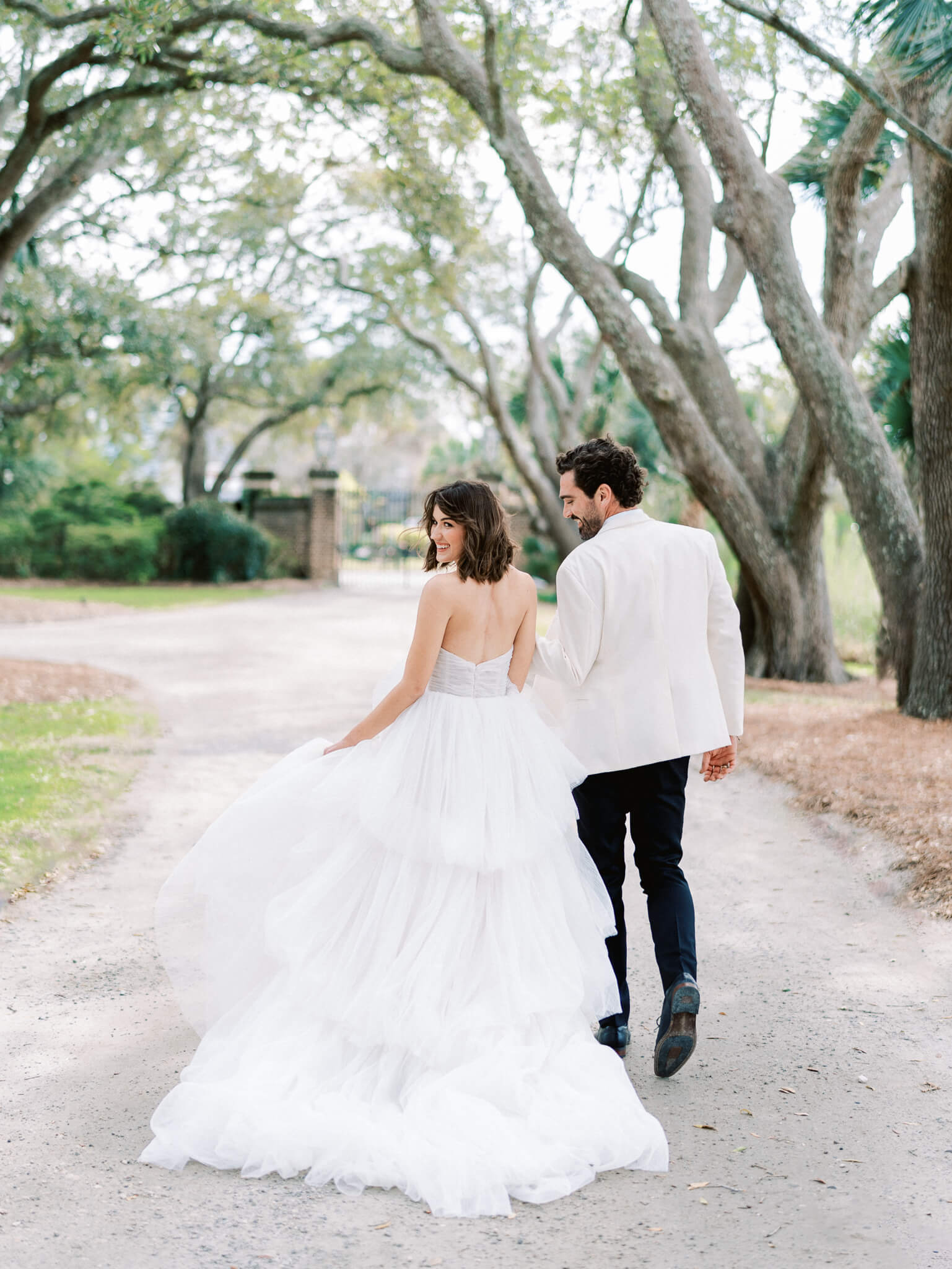 A bride and groom walking away along the sandy path surrounded by live oaks at Lowndes Grove Wedding Venue.