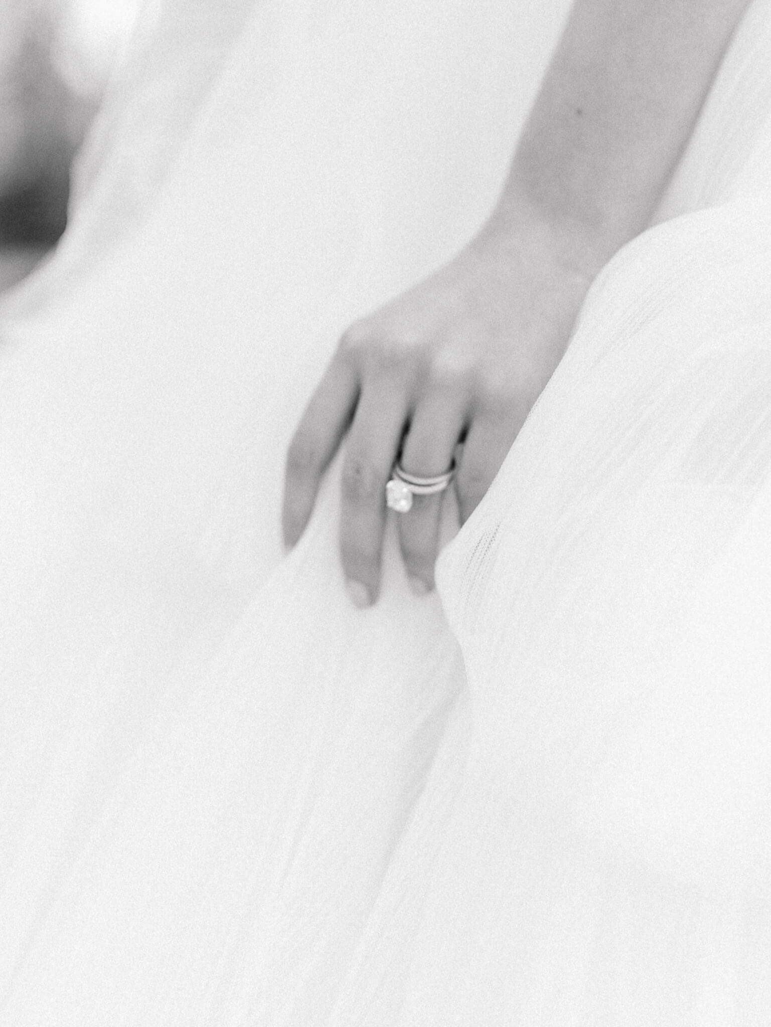 Black and white image of a bride's hand with her engagement and wedding rings grasping her tulle gown.