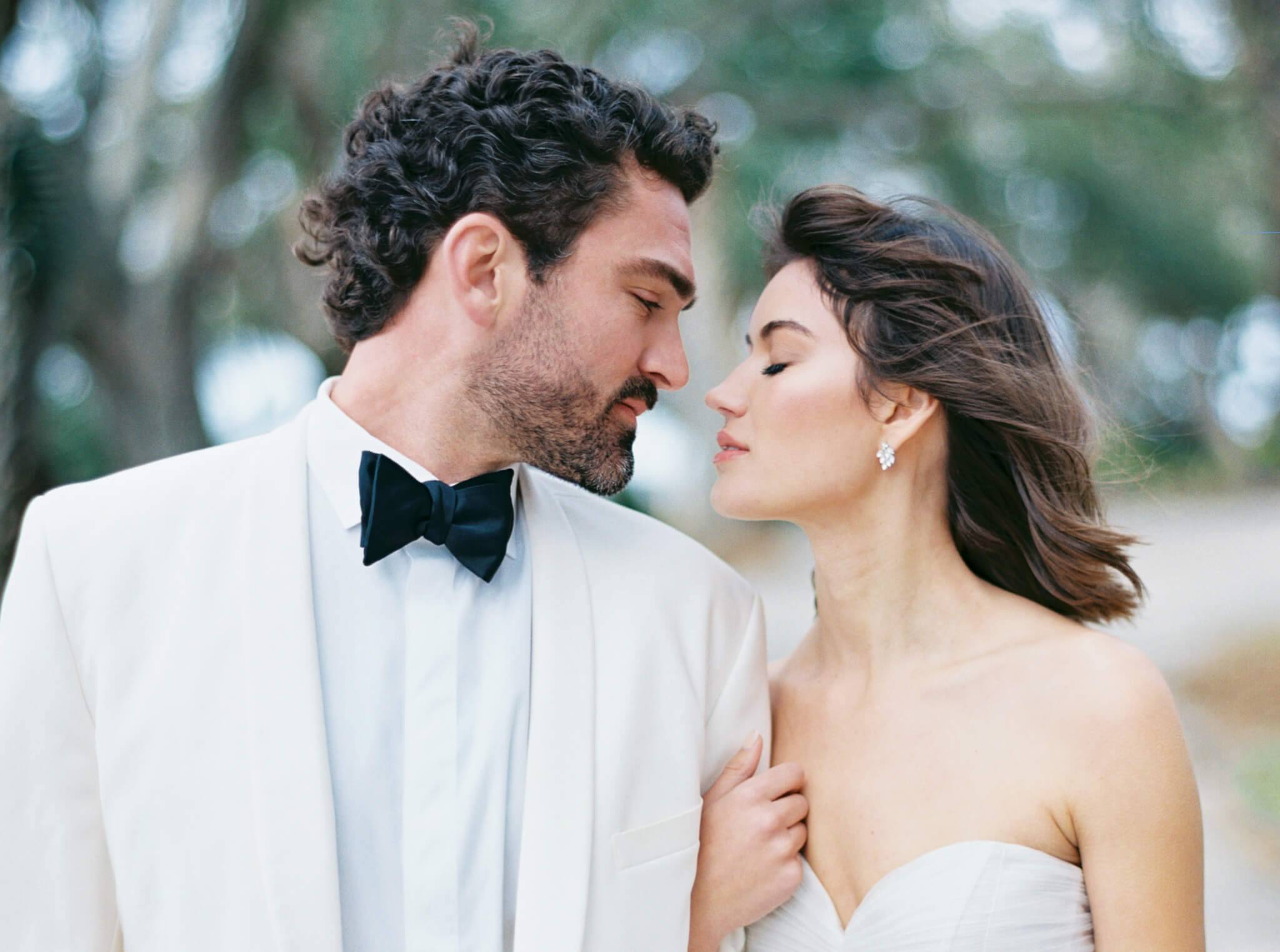 Closeup of a dark haired groom in a white tux and a brown haired bride in a strapless gown about to kiss.
