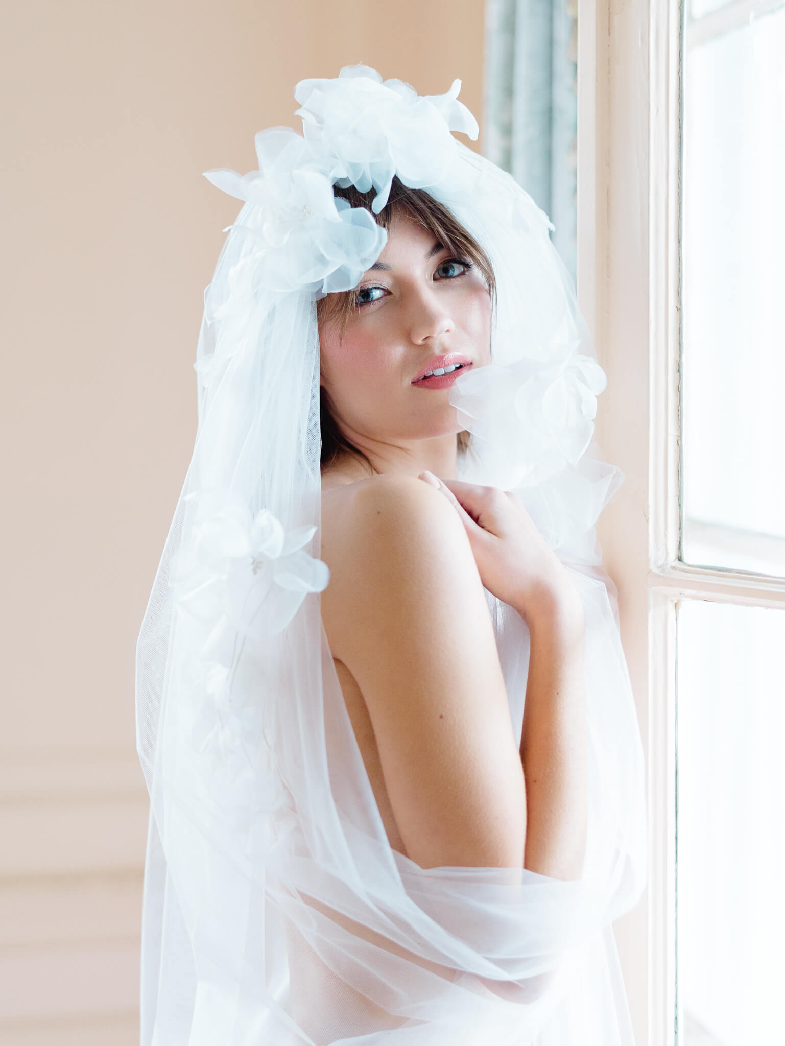 Closeup boudoir image of a bride wrapped in her veil while standing near a window in Lowndes Grove's pink room.