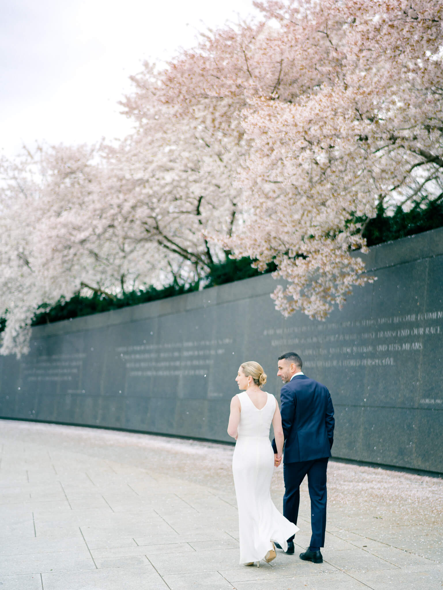 A bride and groom walking under the cherry blossom trees at the MLK Memorial in Washington, D.C.