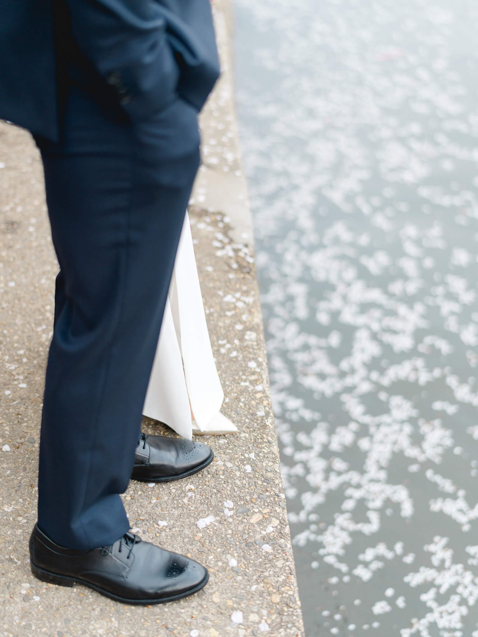 Closeup of a bride and groom's feet standing at the edge of the tidal basin with petals floating in the water