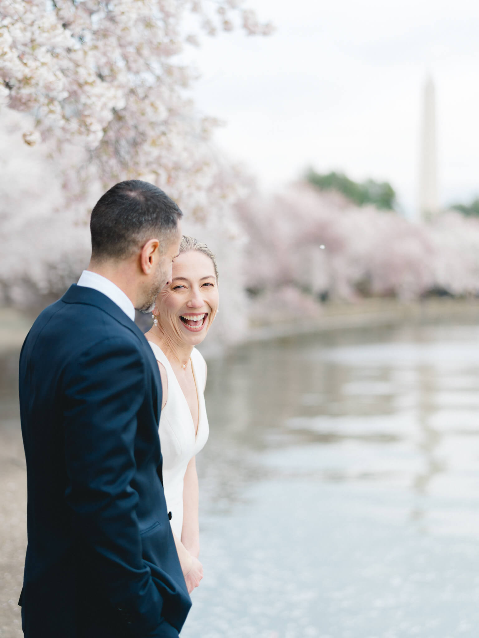 Closeup of a bride laughing while she is standing with her groom at the Tidal Basin with the Washington Monument and cherry blossom trees in the background
