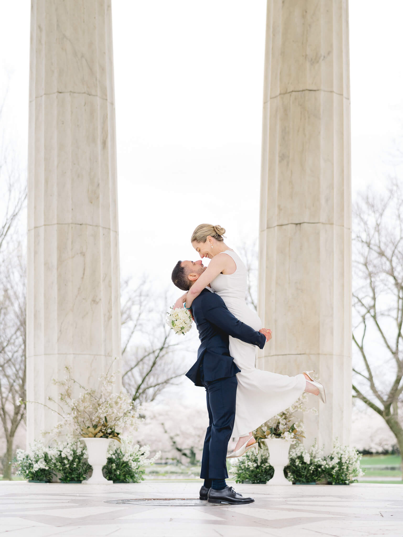 A groom picking up his bride after their cherry blossom elopement at the D.C. War Memorial