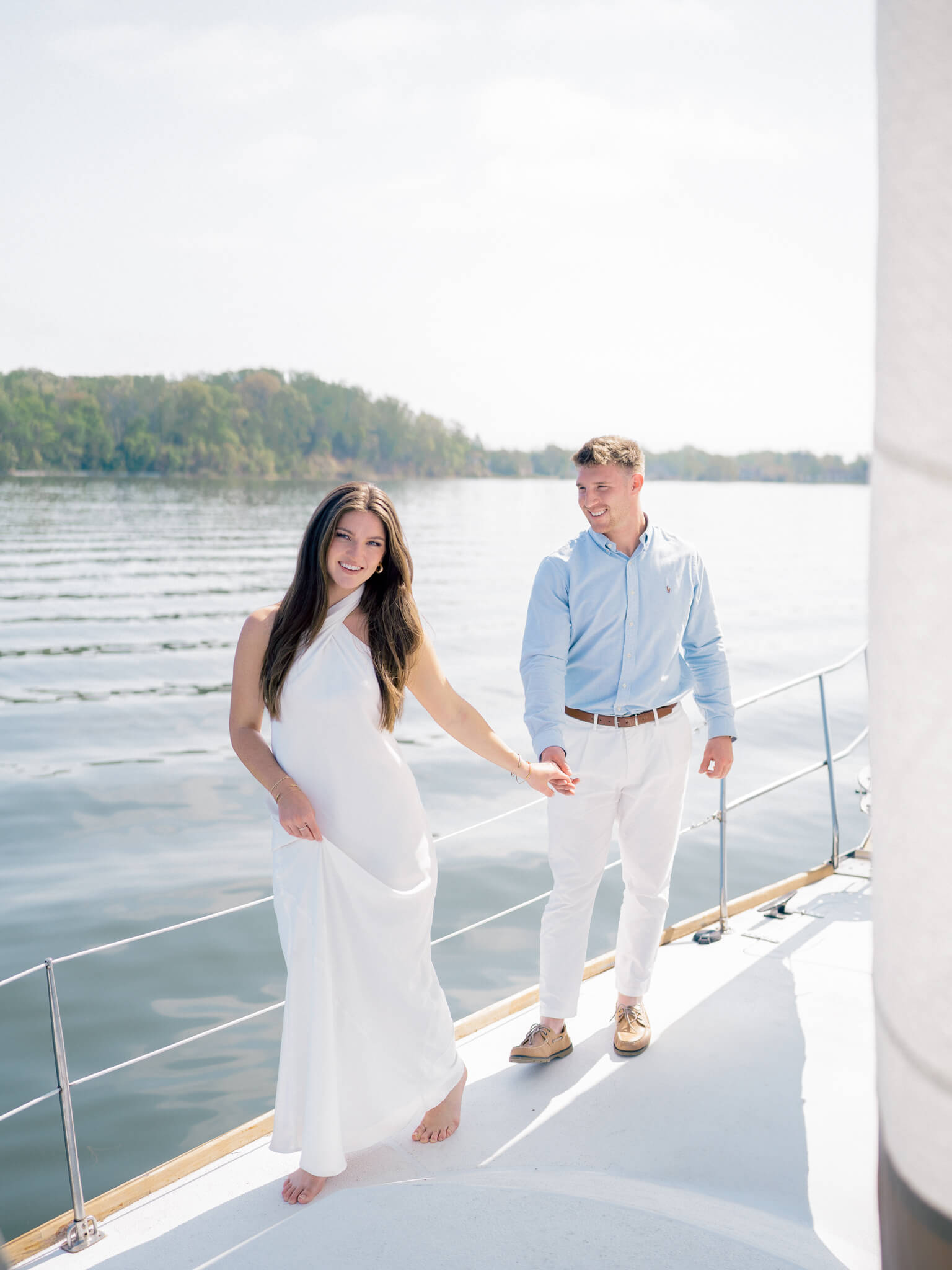 A couple walking hand in hand on a sailboat during their engagement session.
