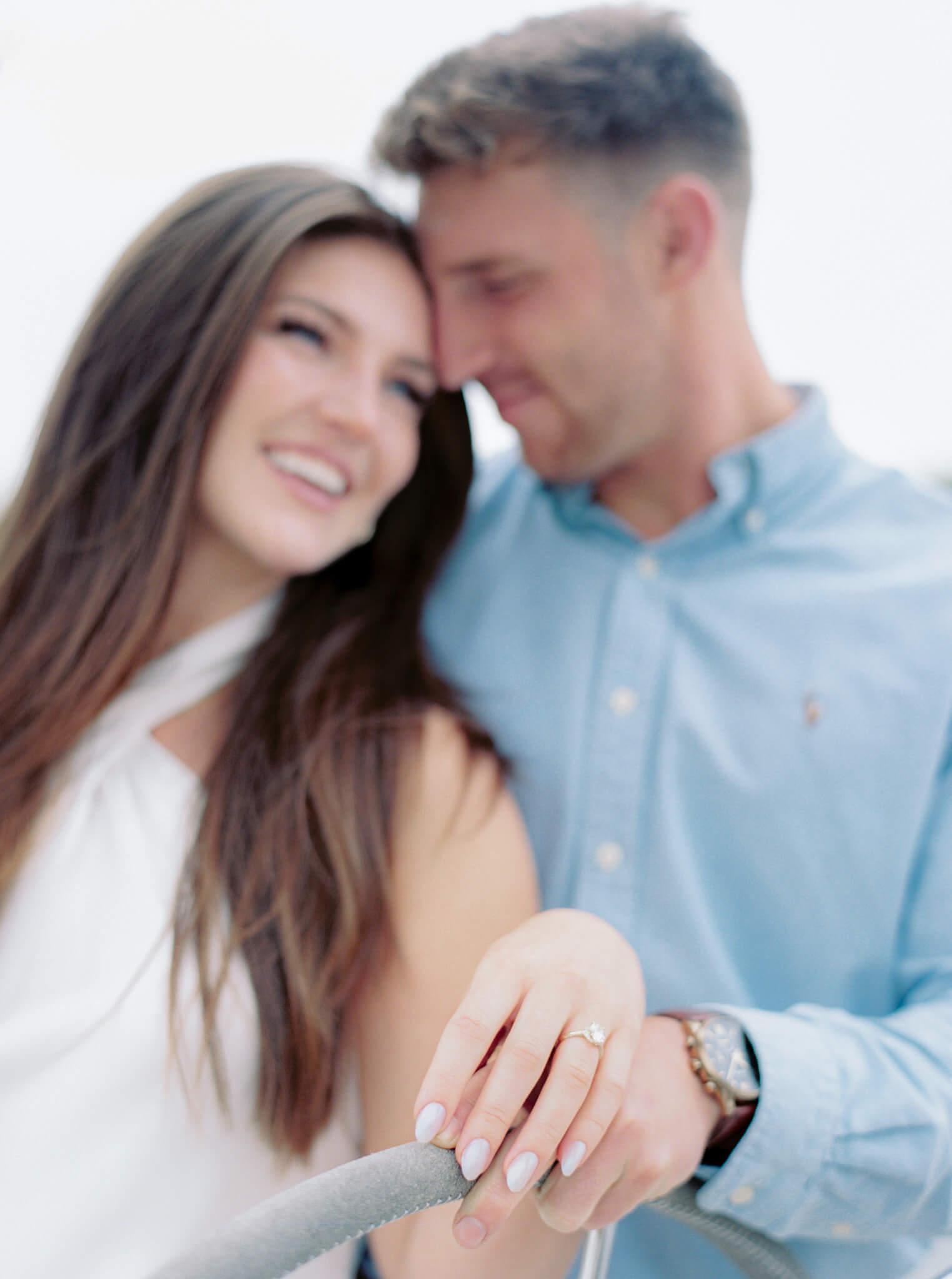 A woman nuzzling into a man during their Annapolis engagement photos while holding the steering wheel of a sailboat.