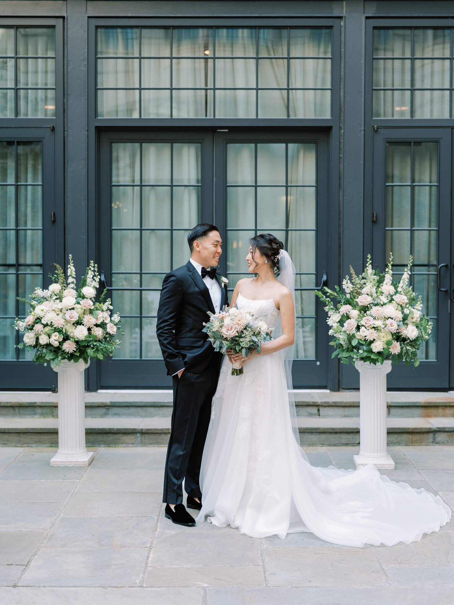 A bride and groom standing at the altar arm in arm between two floral centerpieces looking at each other.