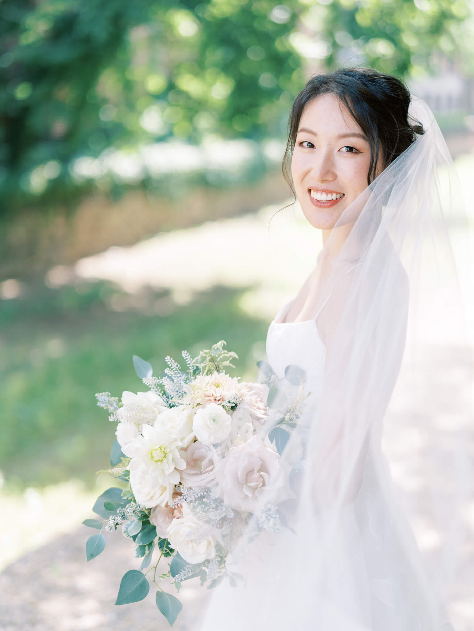 Closeup of a bride looking back over her shoulder in her wedding gown while cradling her blush and cream bouquet.