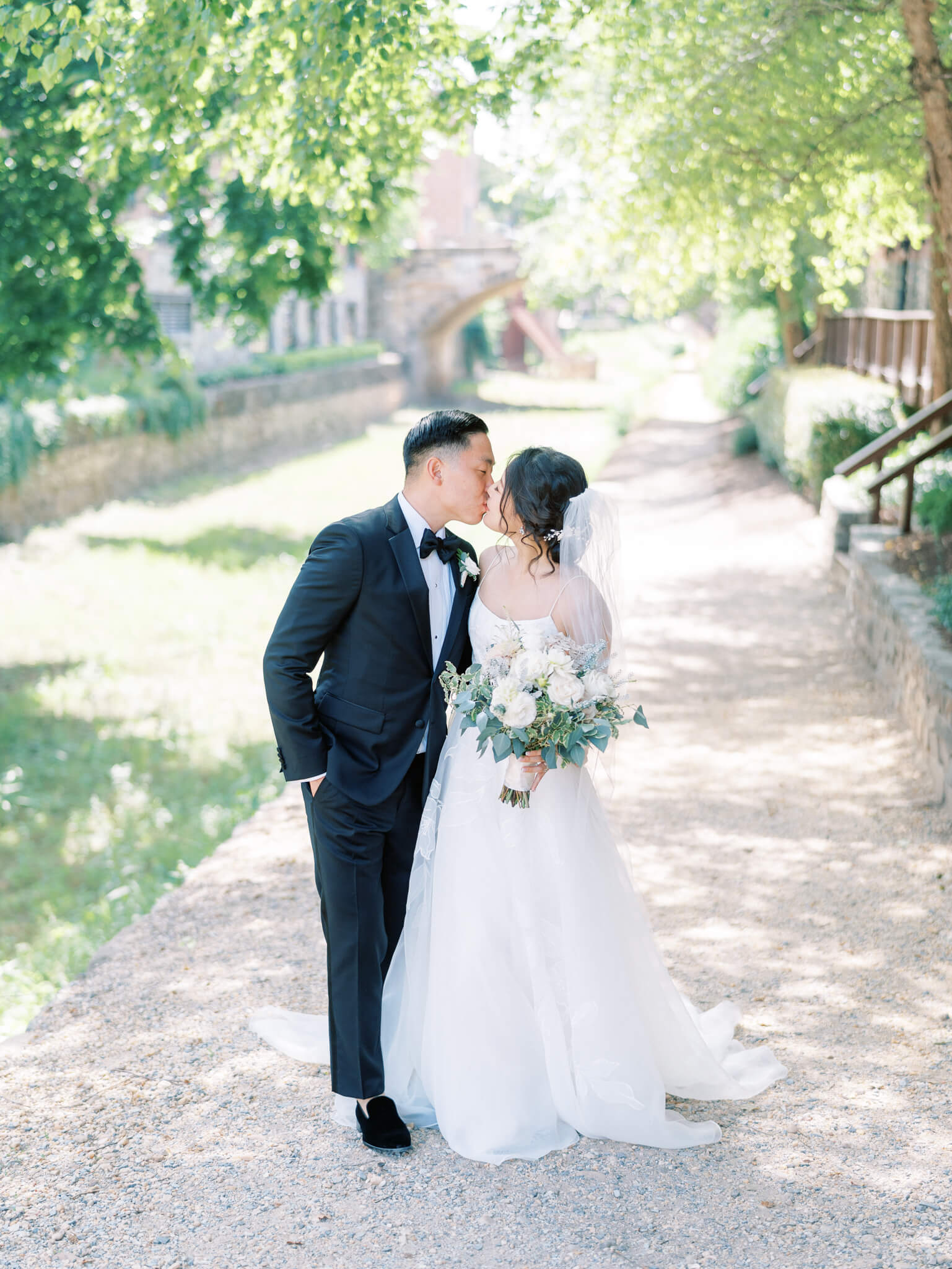 A groom in a black tux kissing his bride in her wedding gown at the canal in Georgetown on their wedding day.