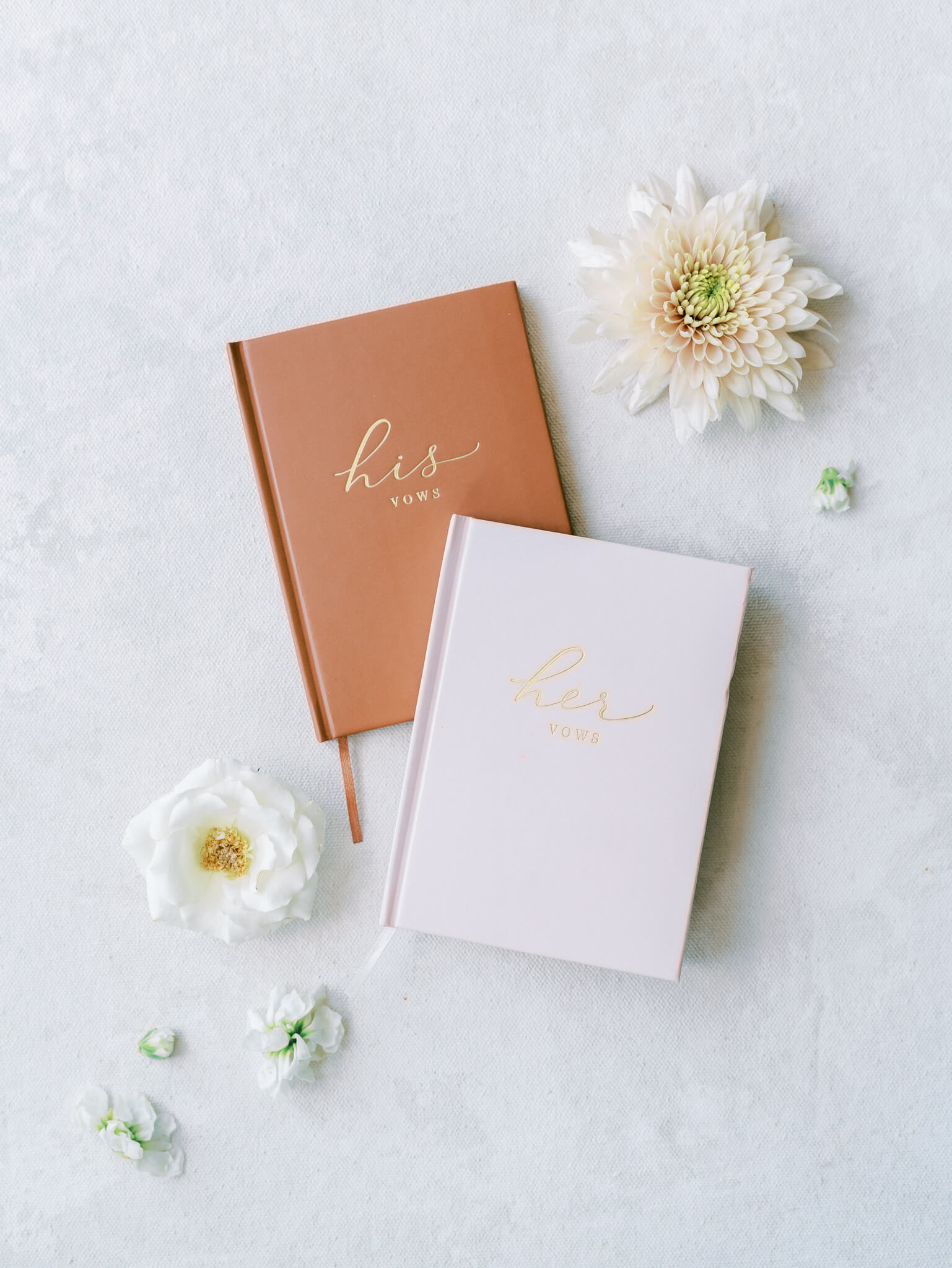 Flatlay of brown and blush colored wedding vow books with flowers.