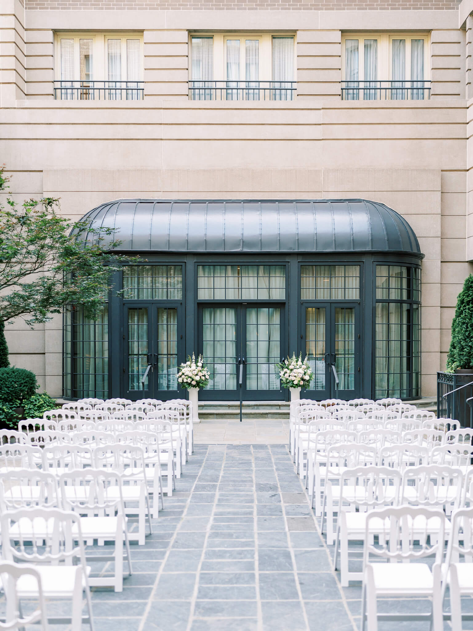 The courtyard of the Westing Georgetown set up for a ceremony with white chairs and floral centerpieces on columns. 