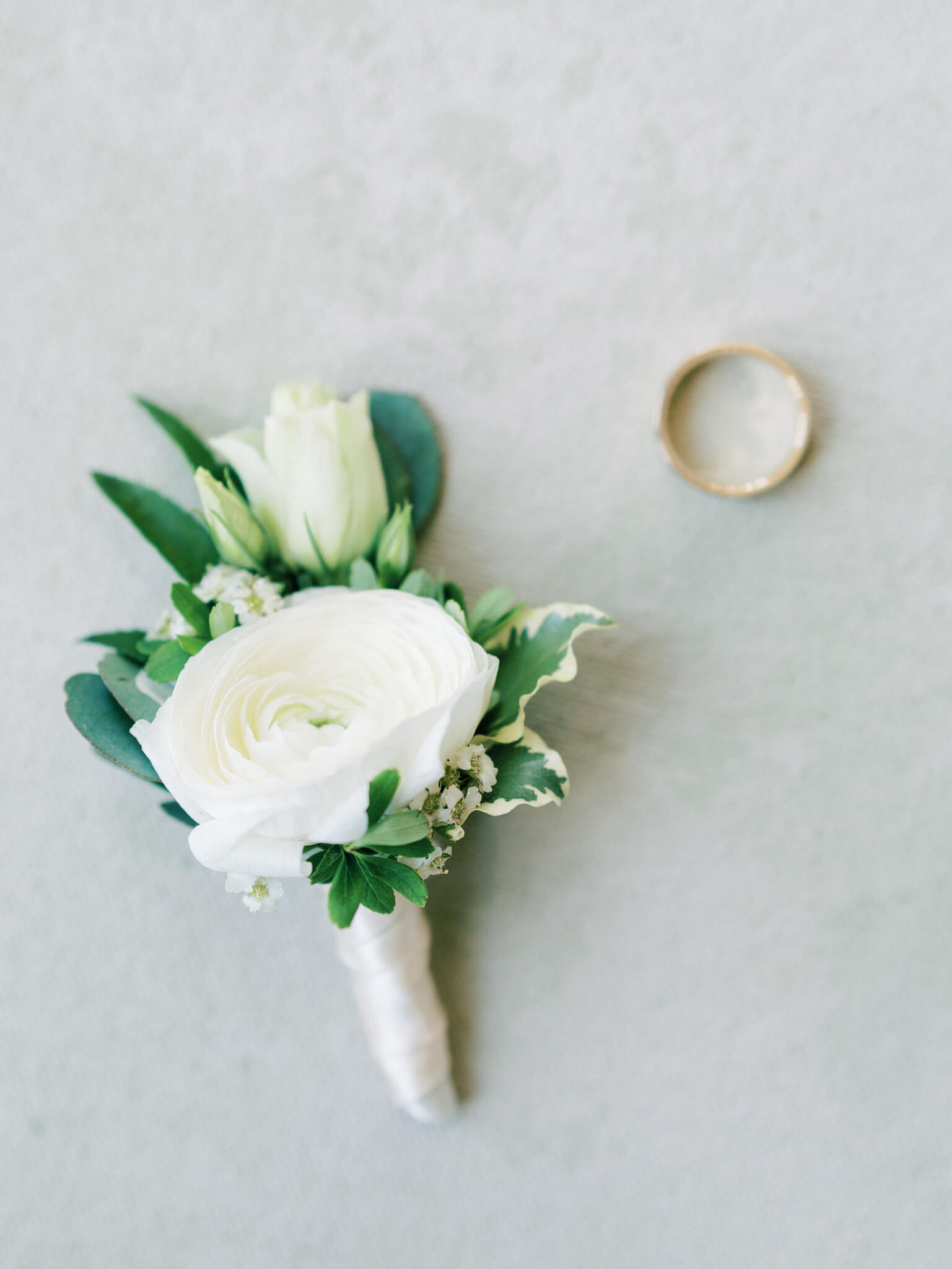 Flatlay of a groom's white and green boutonnière and his gold wedding band.