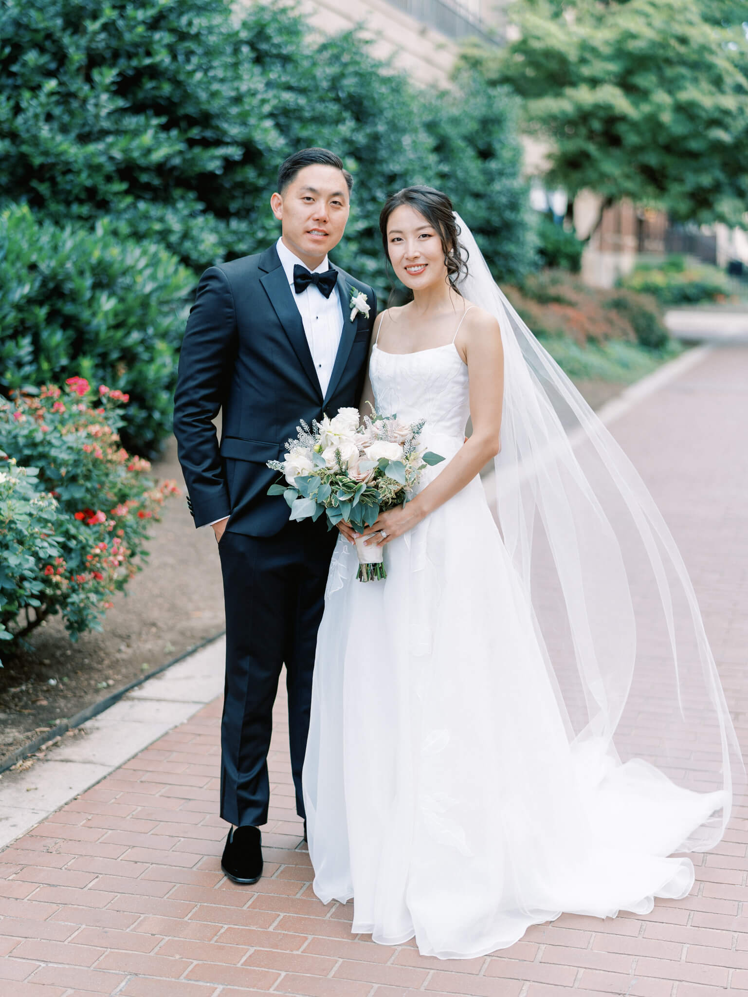 A bride and groom standing arm in arm and holding a bouquet on the sidewalk at the Westin Georgetown.