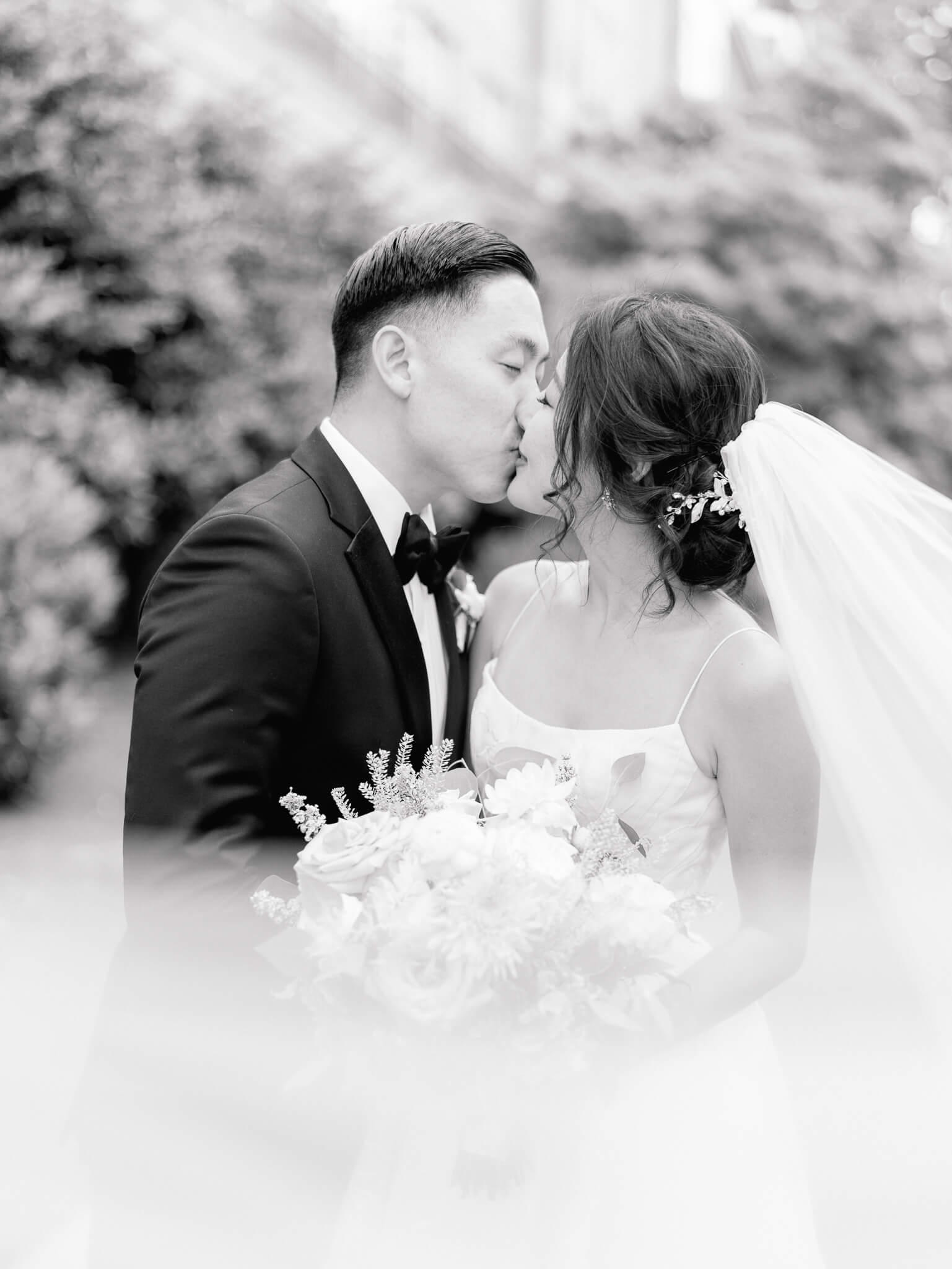 Black and white image of a bride and groom kissing while her veil blows around them at their Westin Georgetown Wedding.