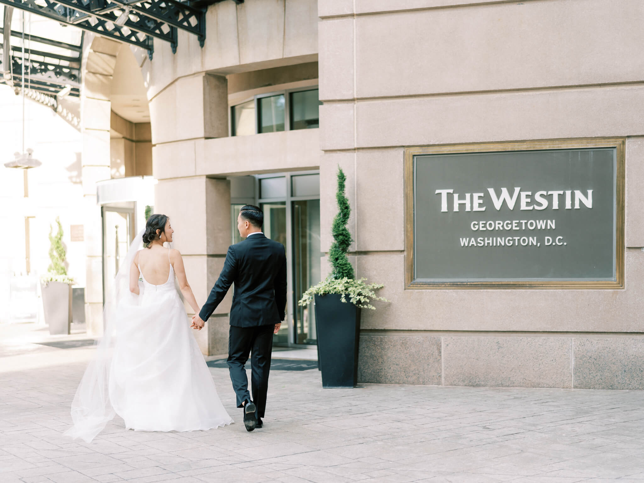 A bride and groom walking hand in hand into the Westin Georgetown in Washington, D.C.