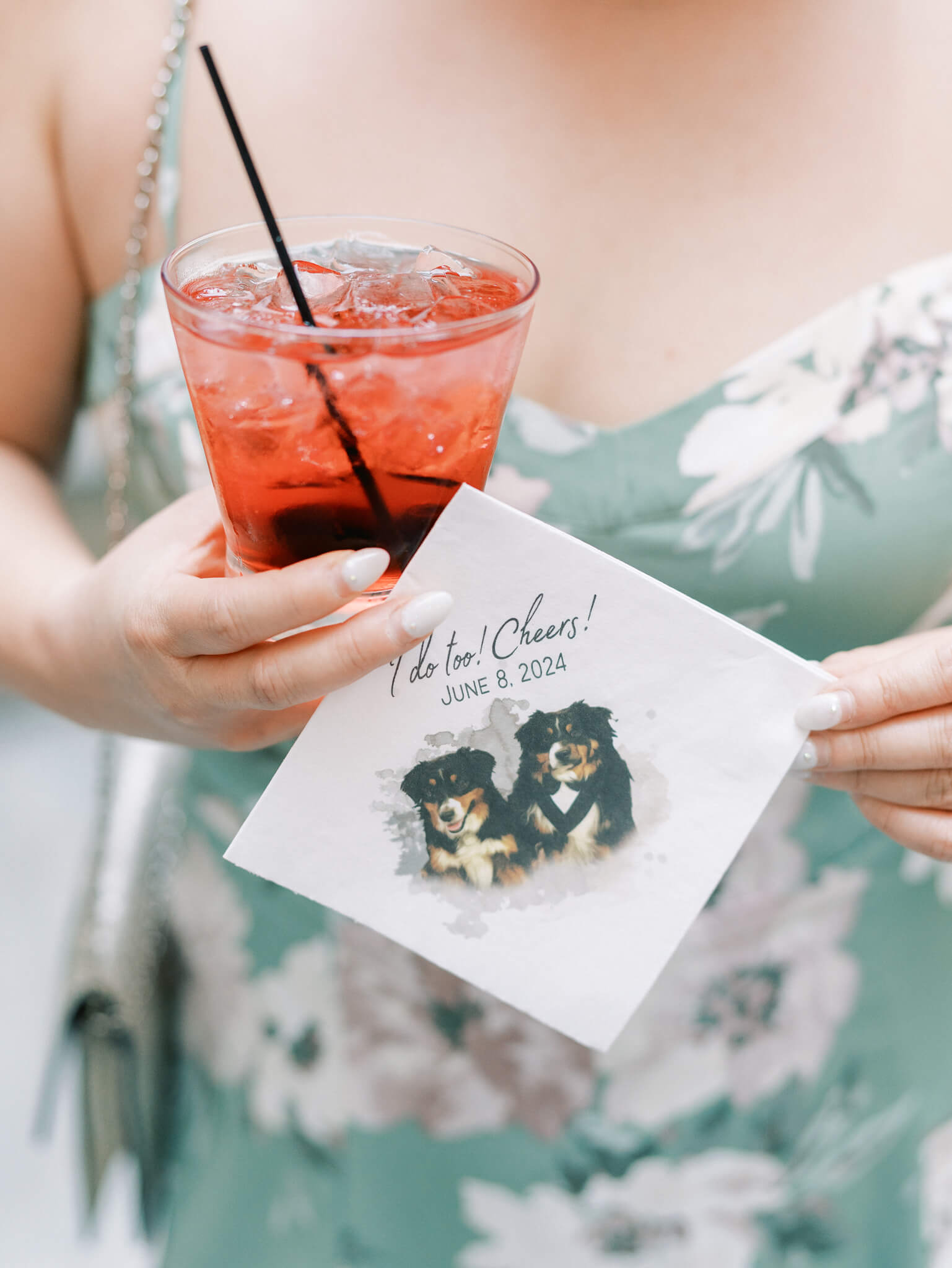 Closeup of a female guest in a green dress with white flowers holding a red drink and napkin with dogs on it at a Westin Georgetown Wedding.