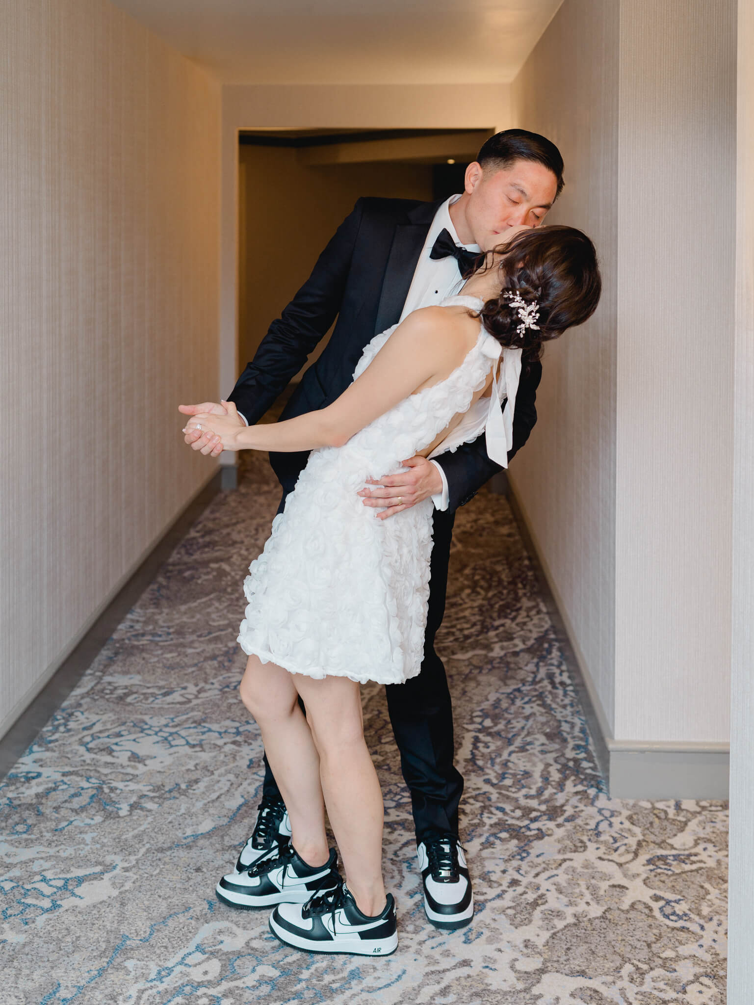 A groom in a tux dip kissing a bride wearing a short dress in the hallway of the Westin Georgetown.