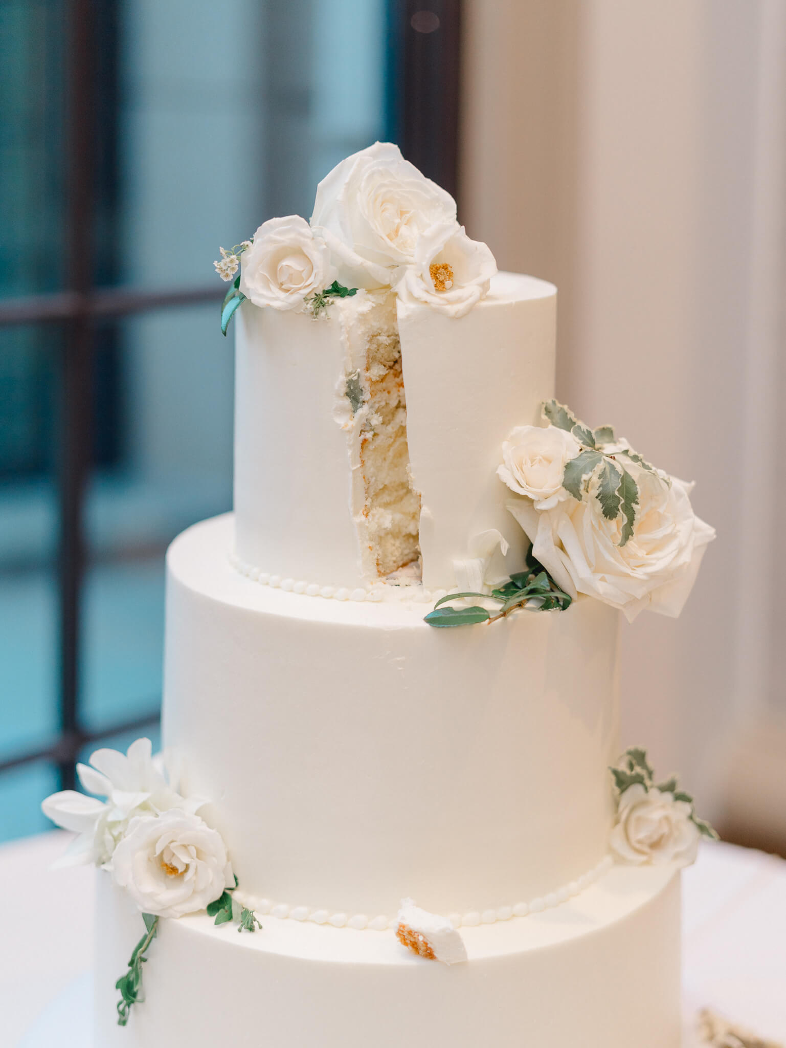 A white wedding cake with a slice missing after the bride and groom cut it.