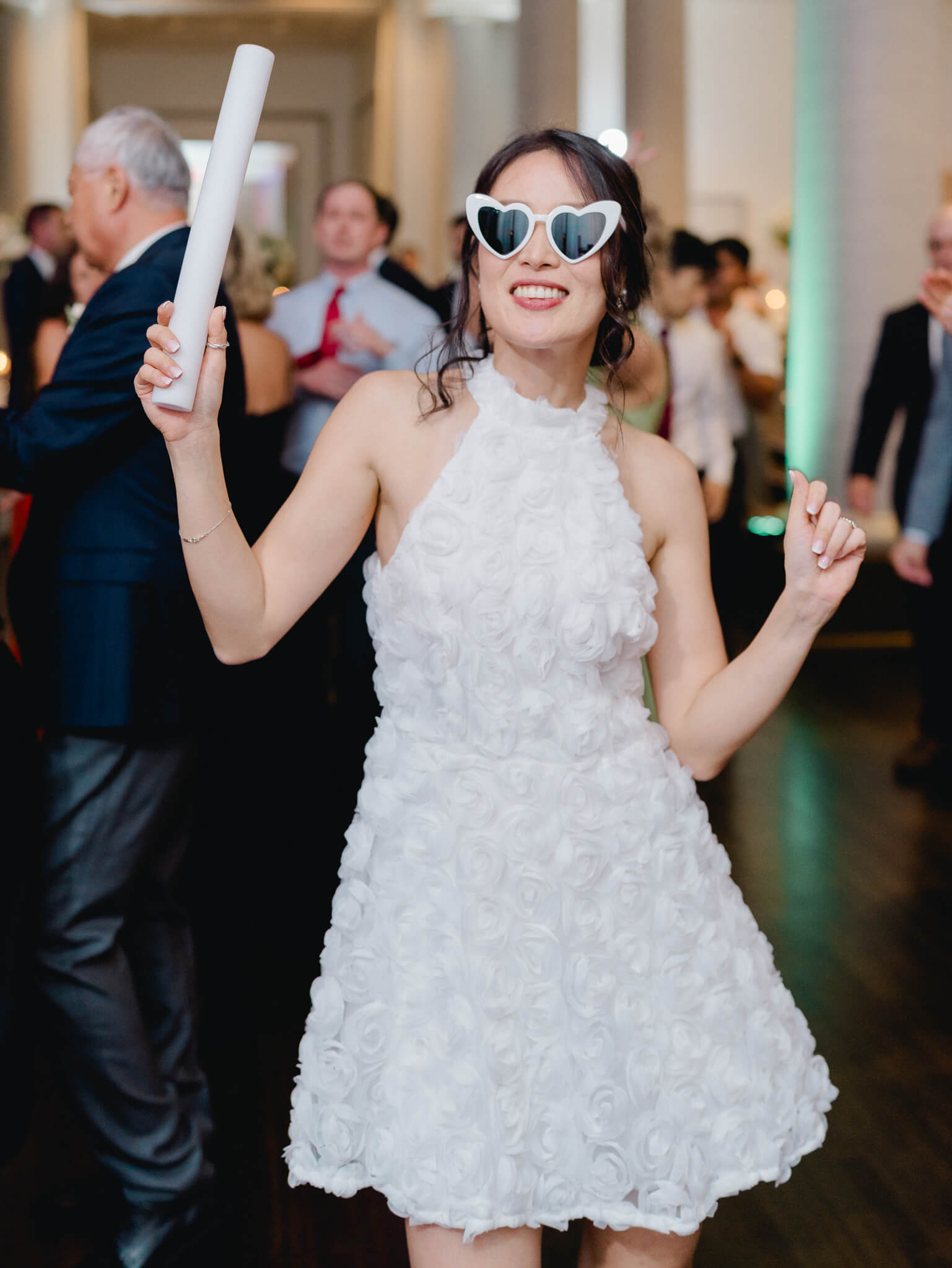 A bride wearing a short dress and sunglasses dancing at her wedding.