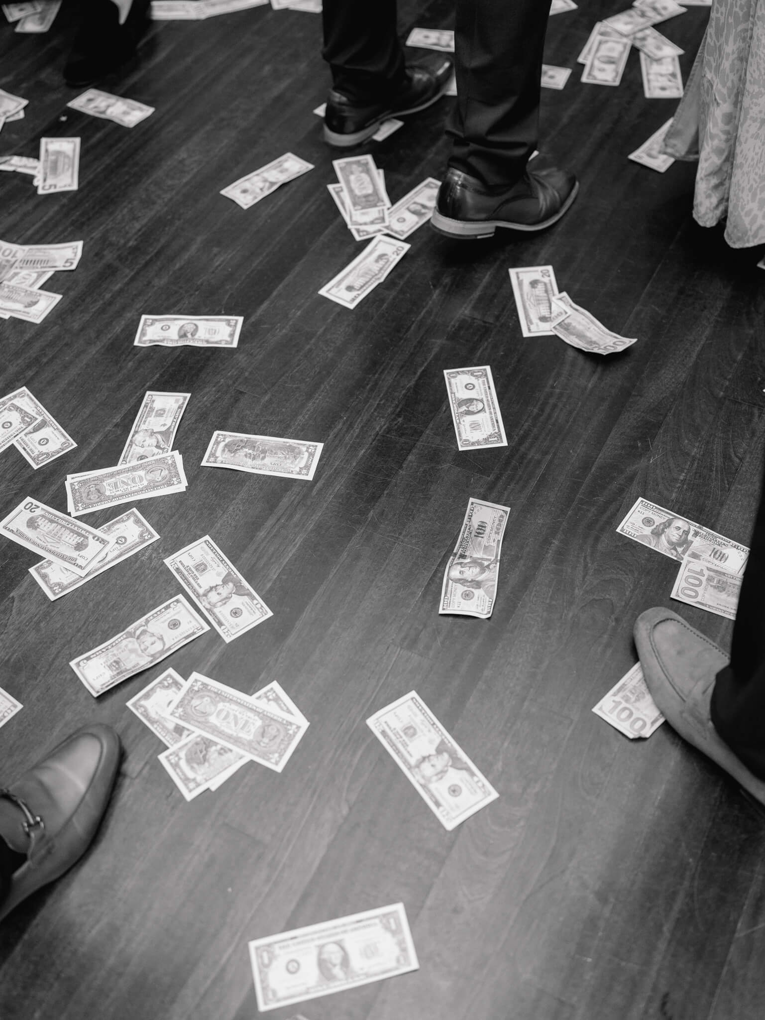 Black and white image of money on the floor and guests' feet dancing.