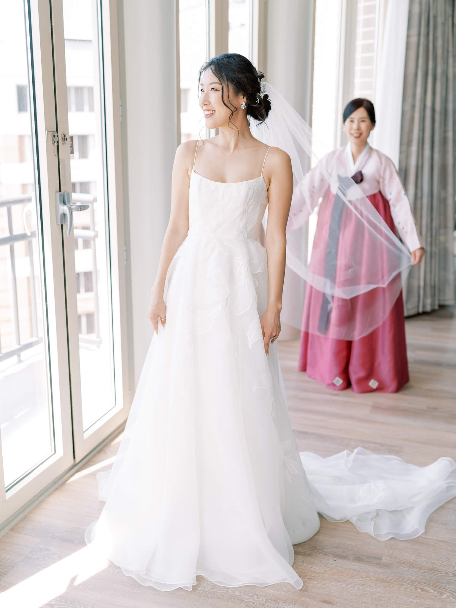 An aunt wearing a pink Korean outfit fluffing the bride's veil in the wedding suite at the Westin, Georgetown.