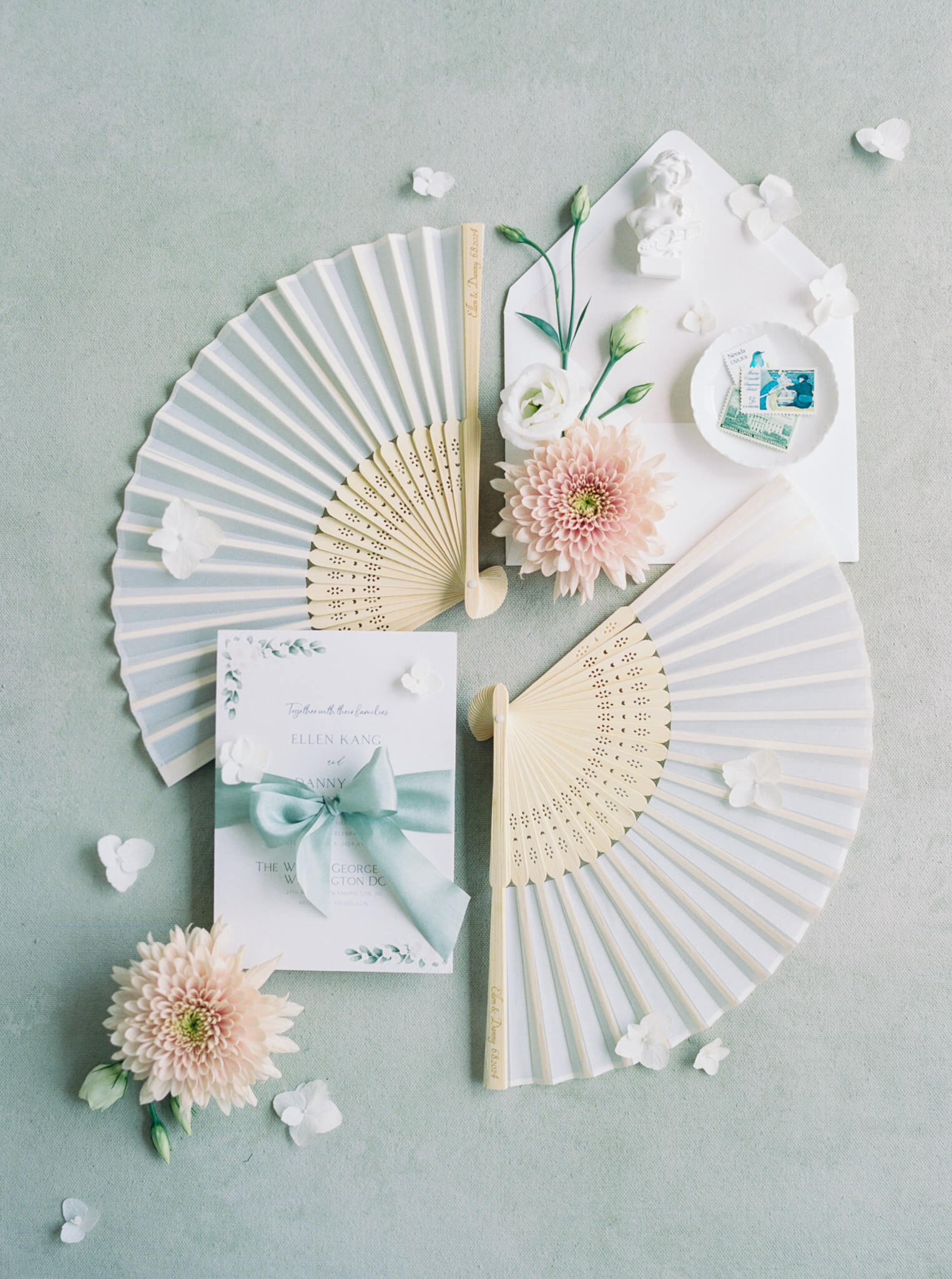 A wedding flatlay with fans and an invitation on a minty green backdrop. 