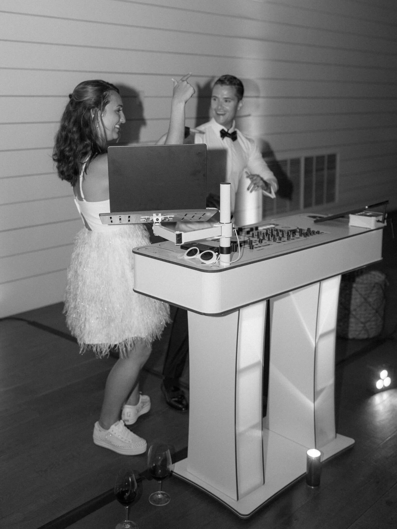 Black and white image of a bride in a short dress and a groom dj'ing their own wedding.