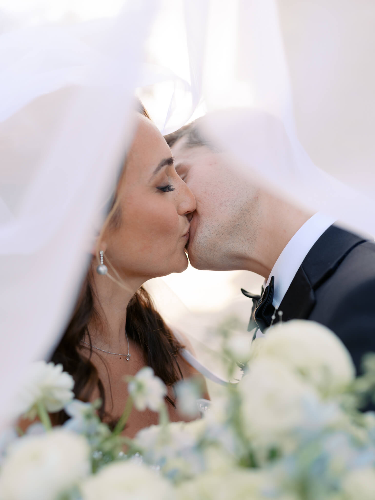 A bride and groom kissing under a veil at their destination wedding weekend.