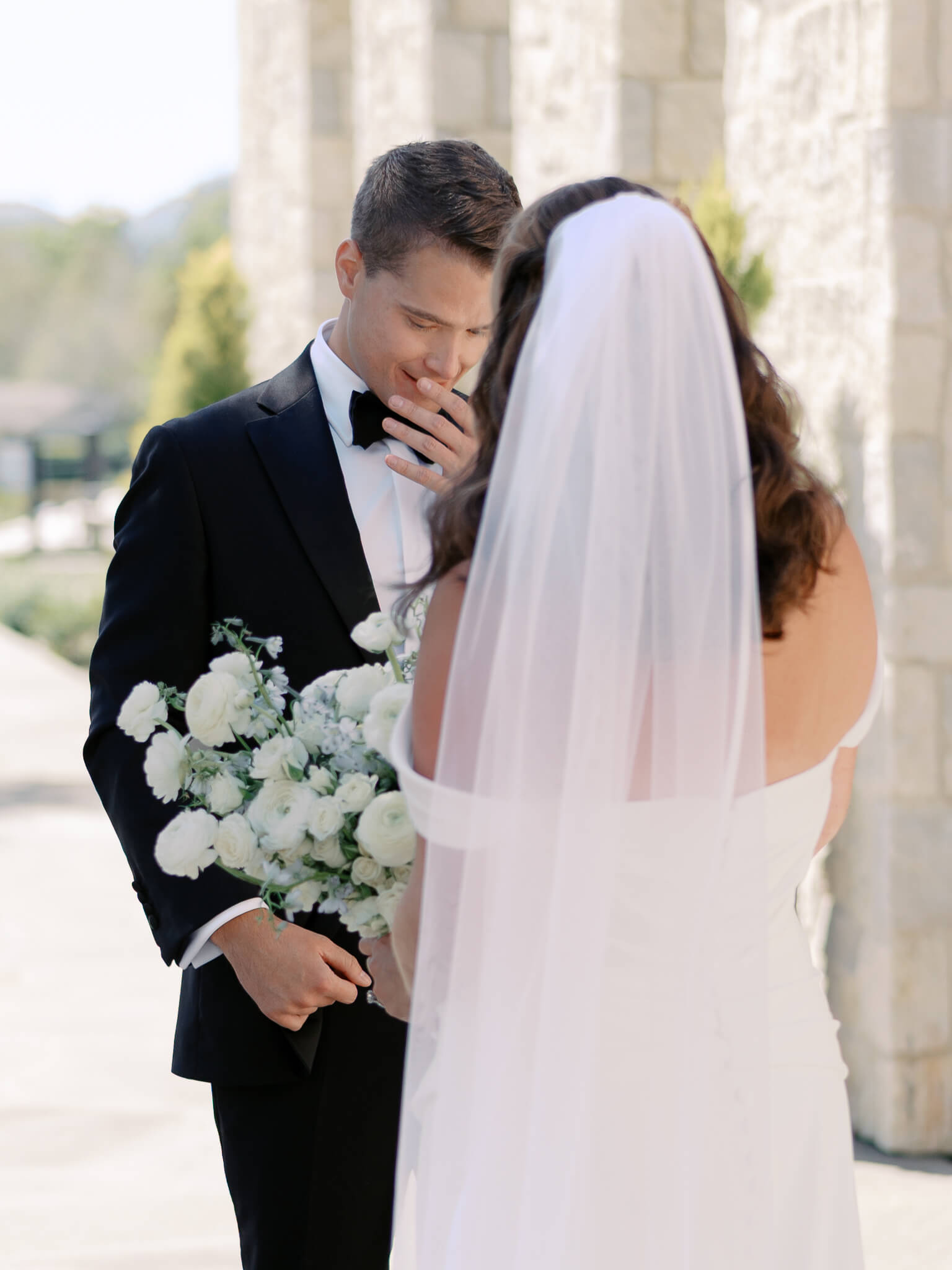 A groom tearing up and raising his hand to his mouth when seeing his bride at their first look.