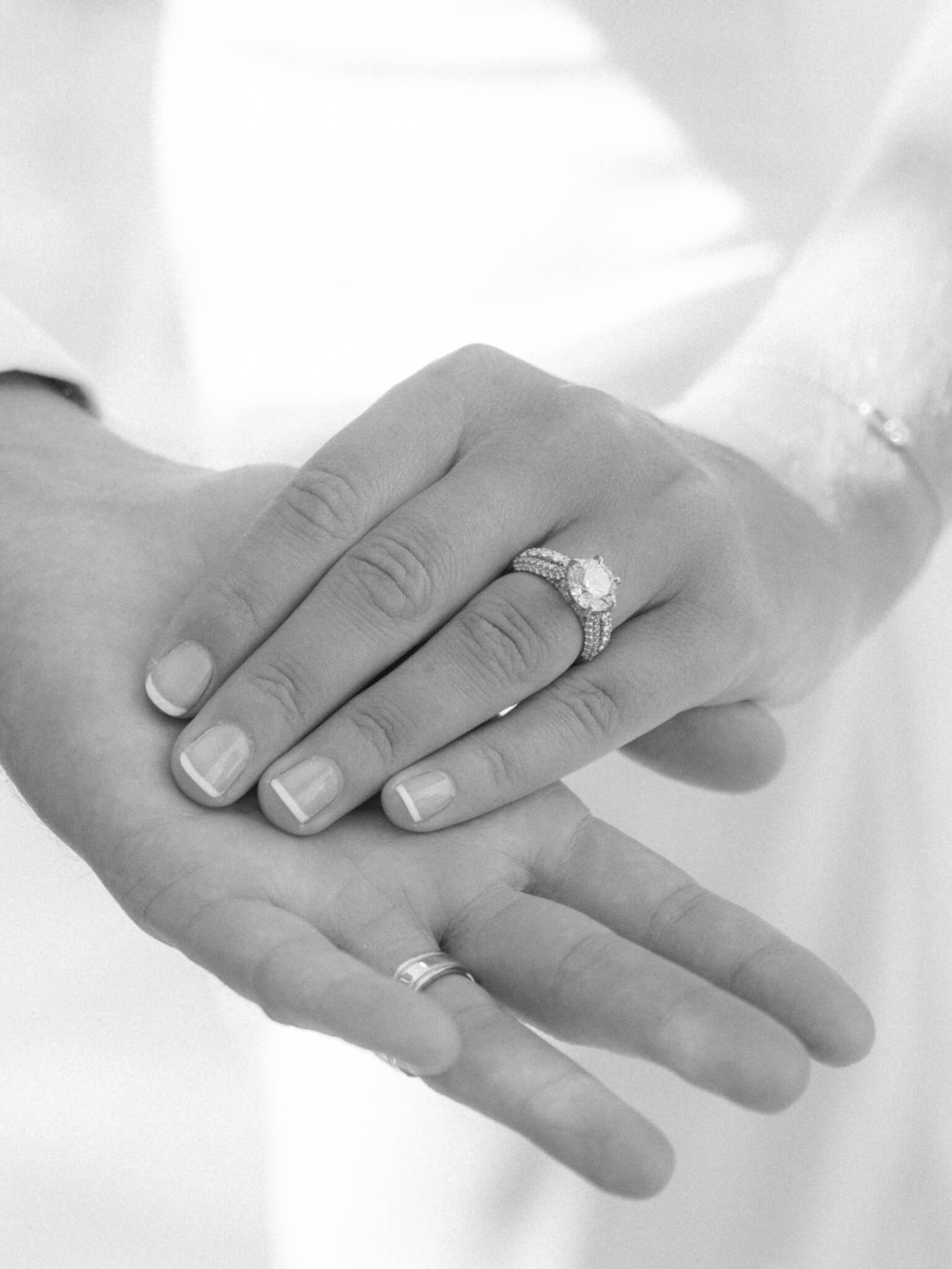 Black and white of a bride and groom's hands showing off their rings.