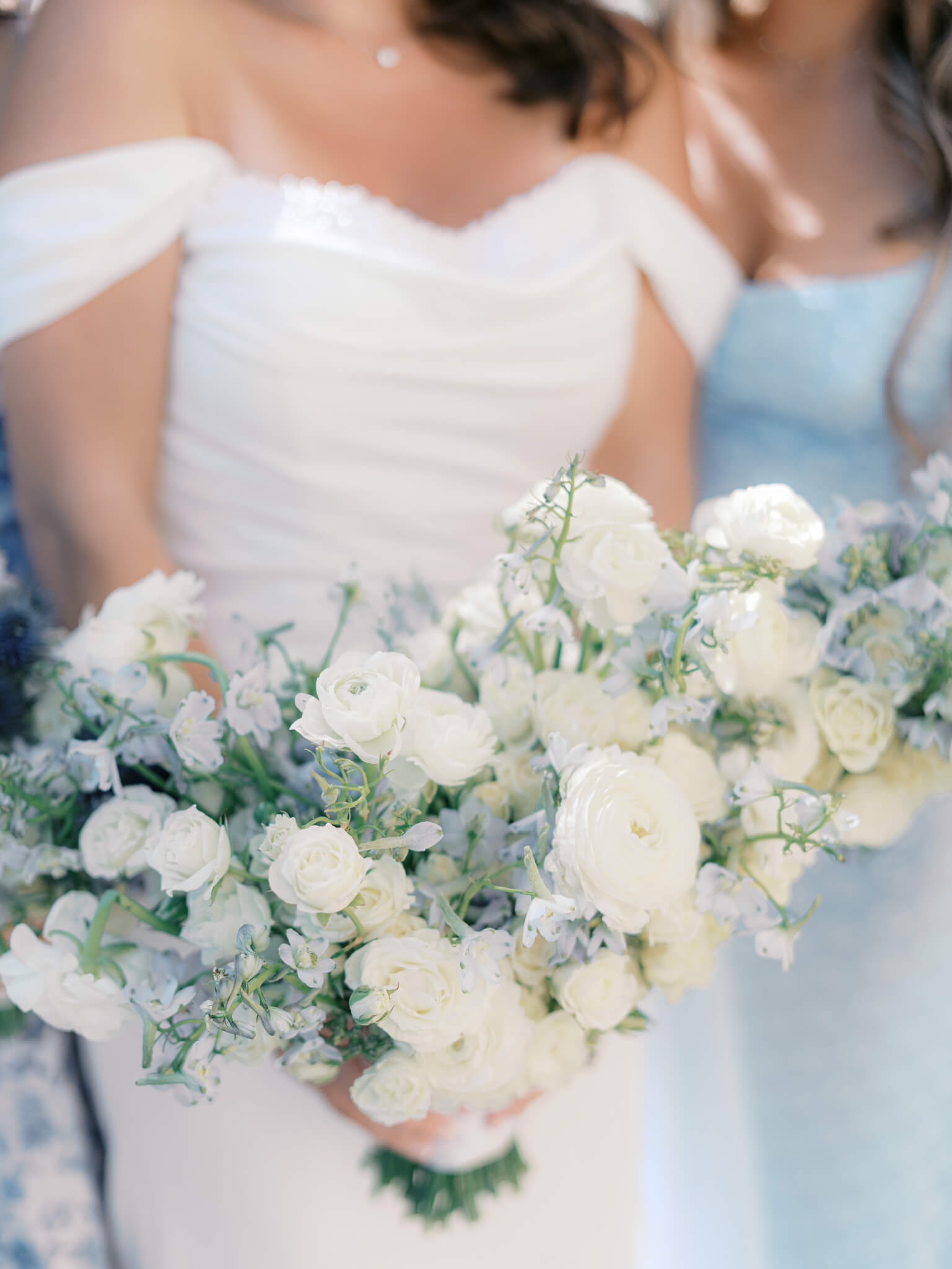 A bride's blue and white bouquet being held between while standing between her bridesmaids.