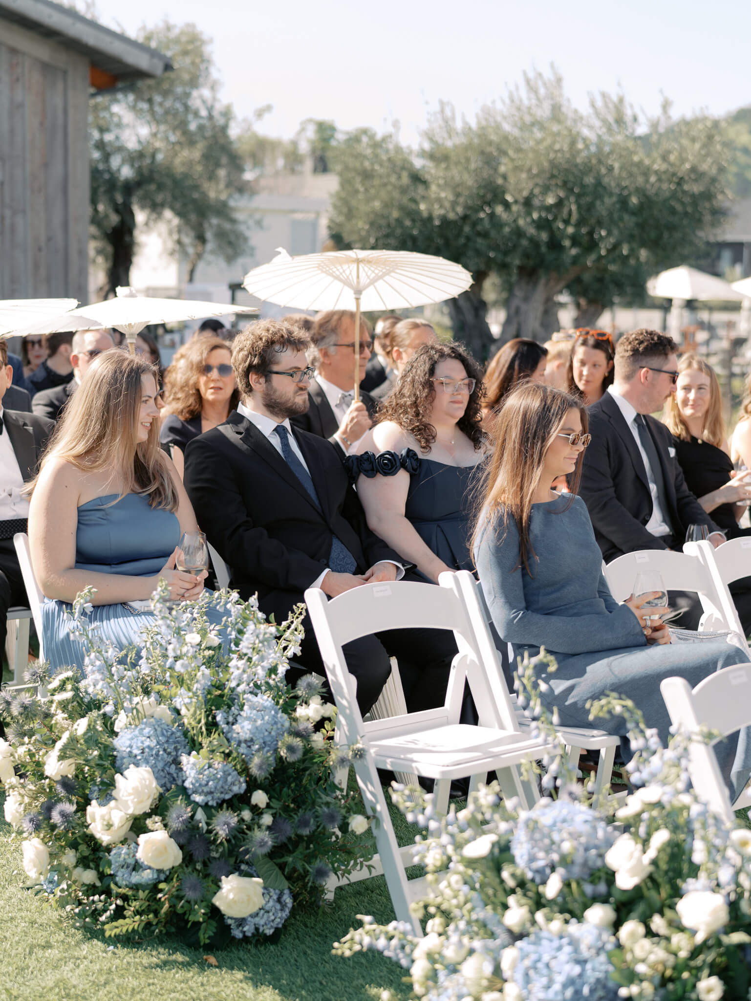 Wedding guests holding parasols seated at a wedding ceremony.