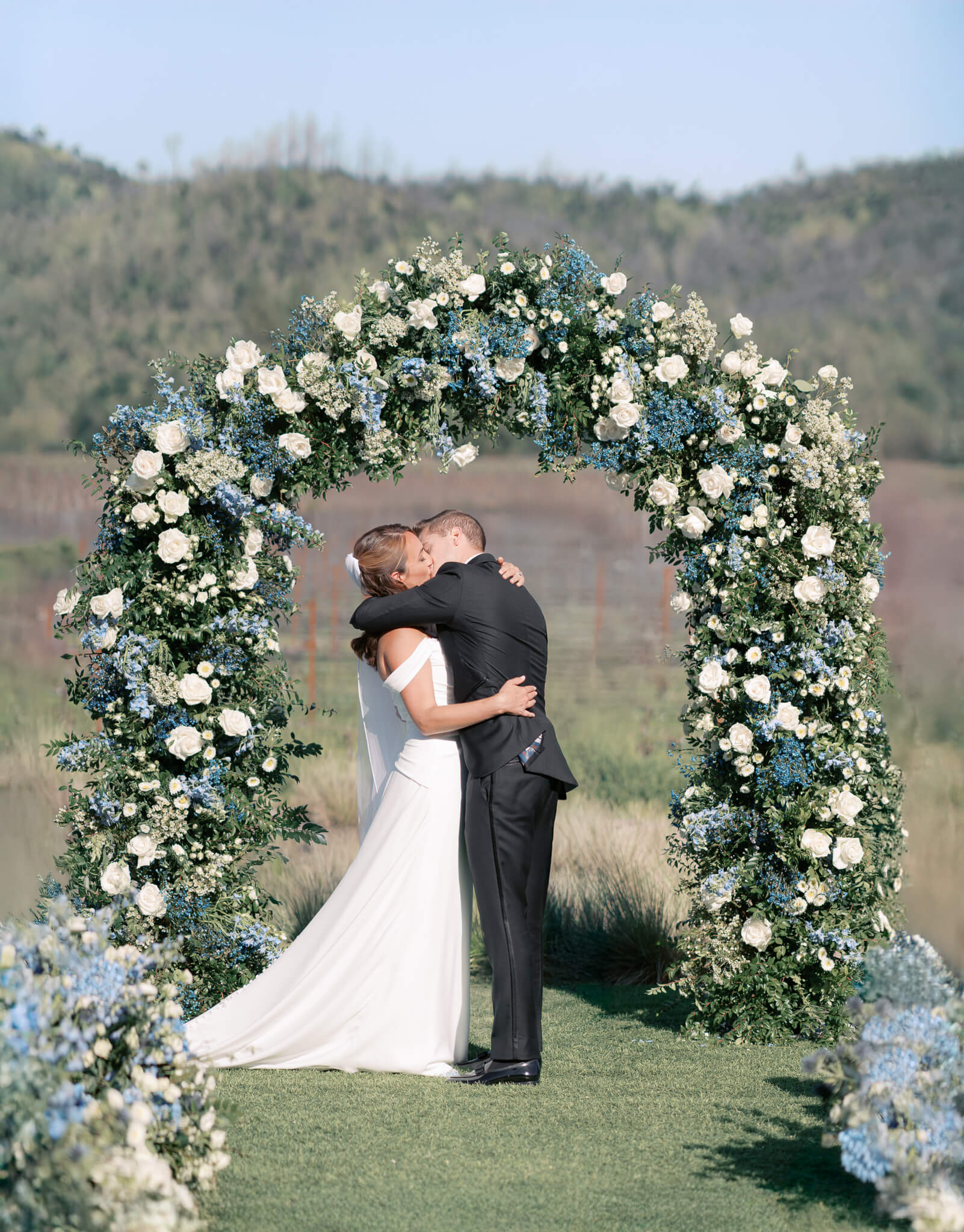 The bride and groom kissing under their blue and white floral arch at their destination wedding ceremony.