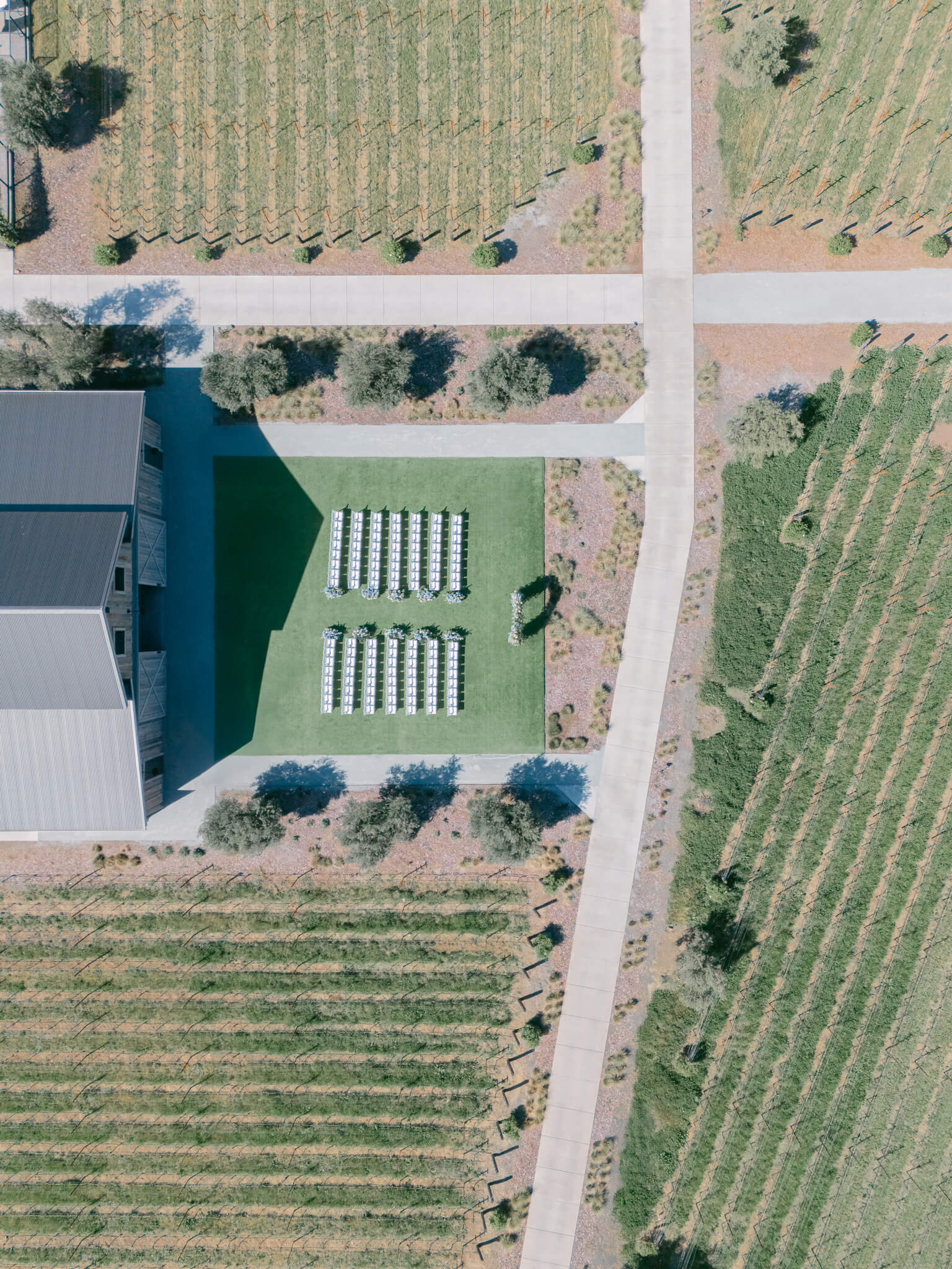 Drone image of a barn building in the middle of a vineyard with a wedding ceremony set up on the lawn.