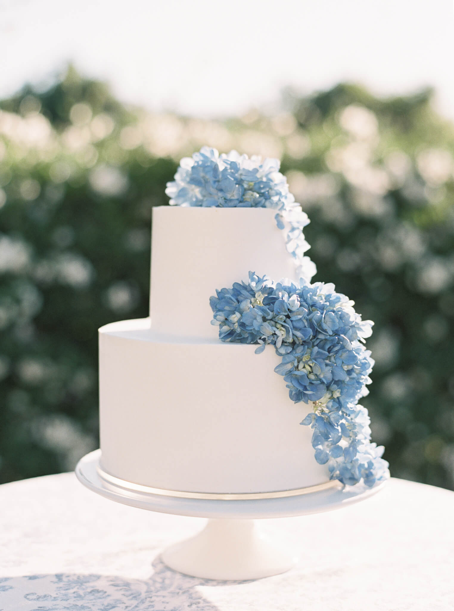 A white two tier wedding cake with blue hydrangeas cascading off the side.