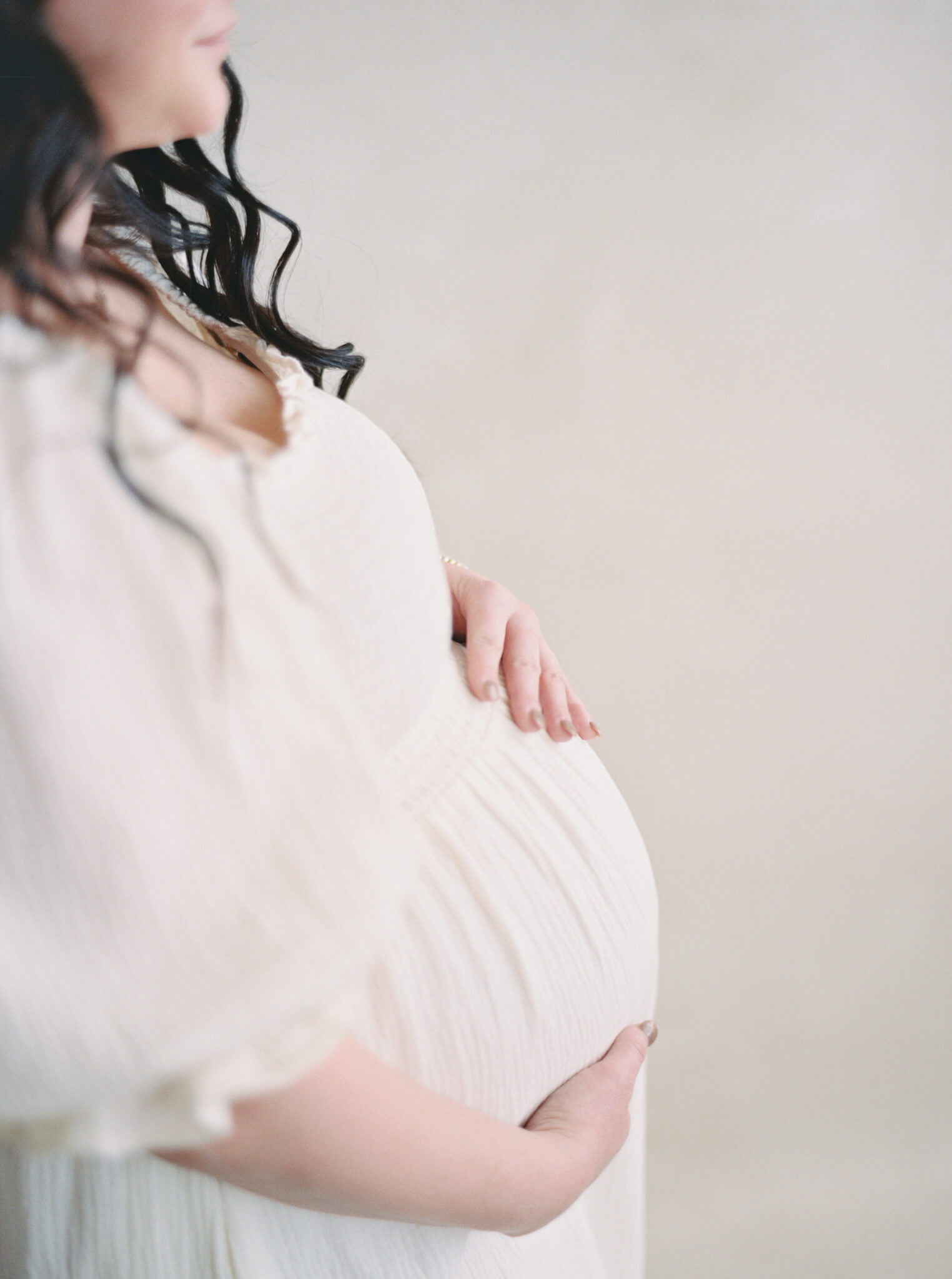 Closeup of a pregnant woman's belly wearing a cream dress for her Annapolis maternity photos.