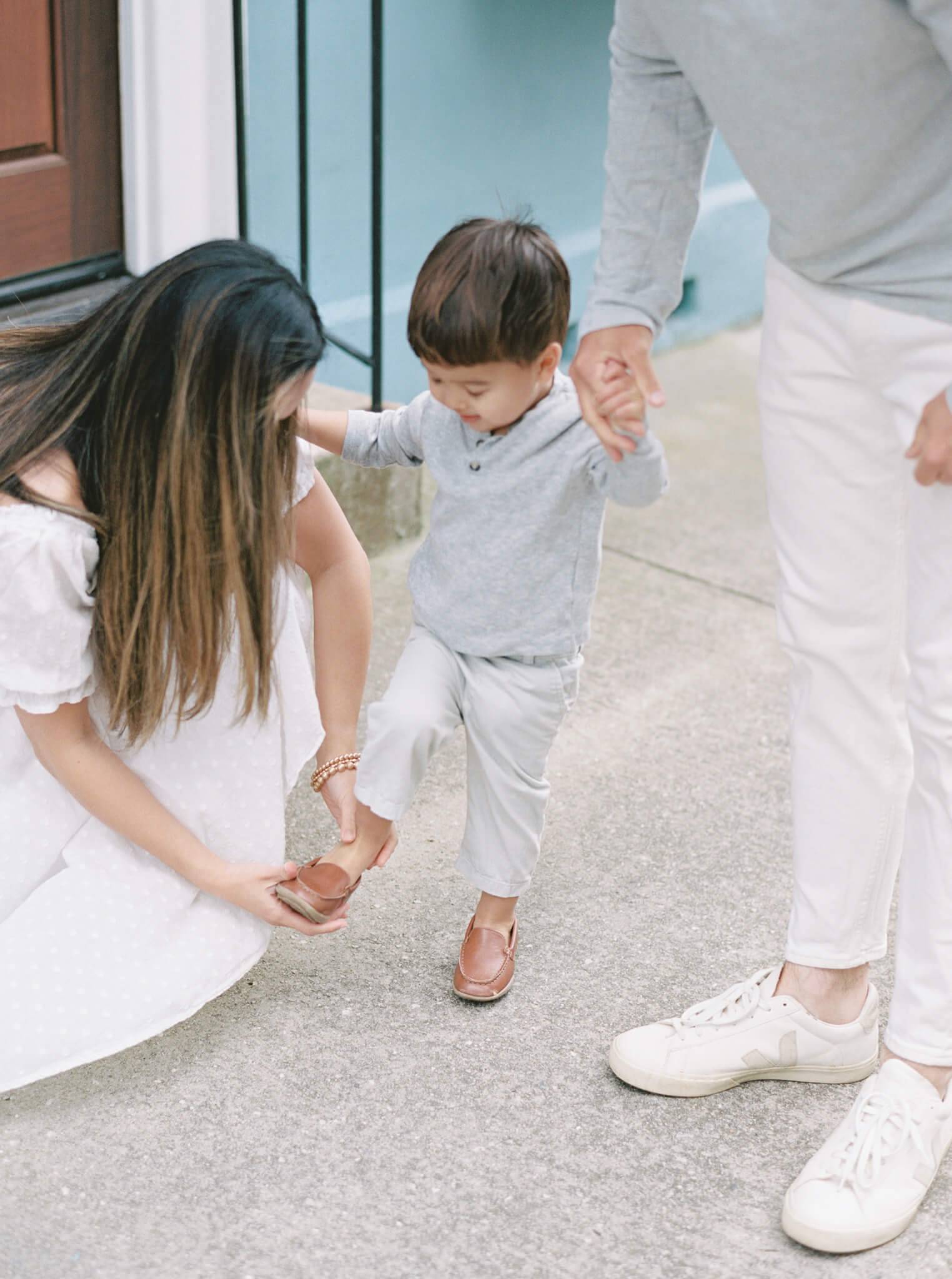 Closeup of a mom bending down and putting her toddler son's shoe back on while dad holds the boys hand.