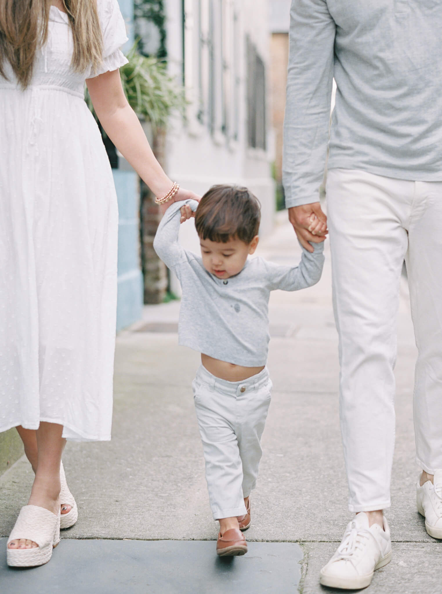 Closeup of a mother and father holding their toddler son's hands while walking during their Charleston Family Photos.