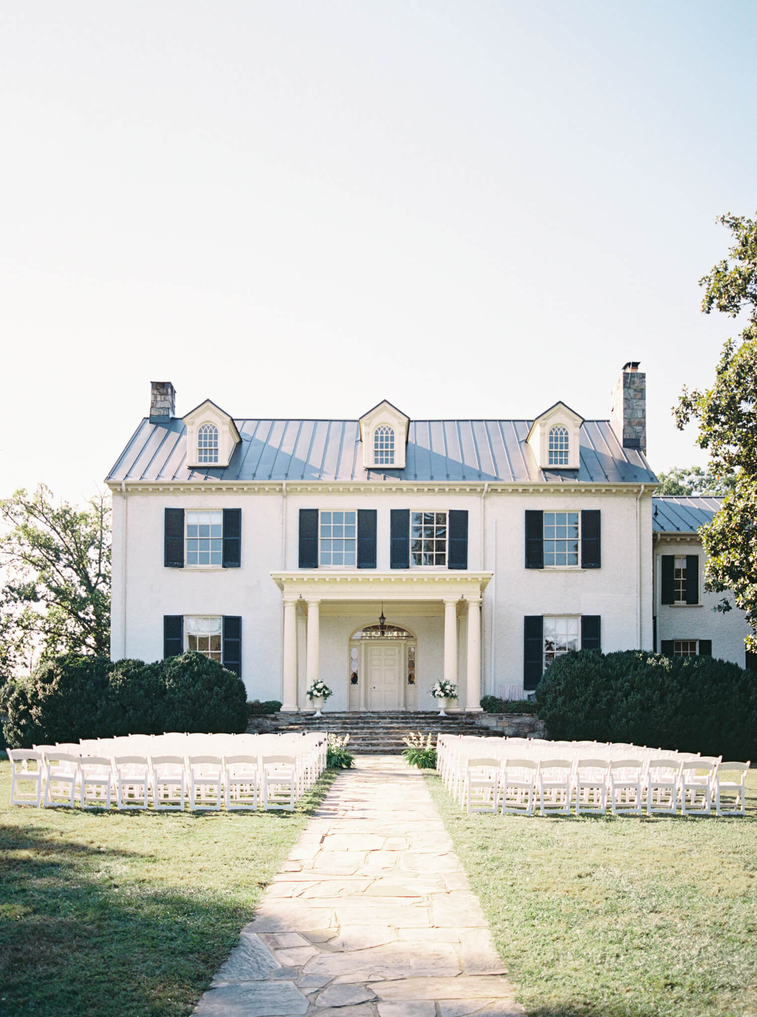 The back of Rust Manor House with white ceremony chairs set up on a sunny afternoon.
