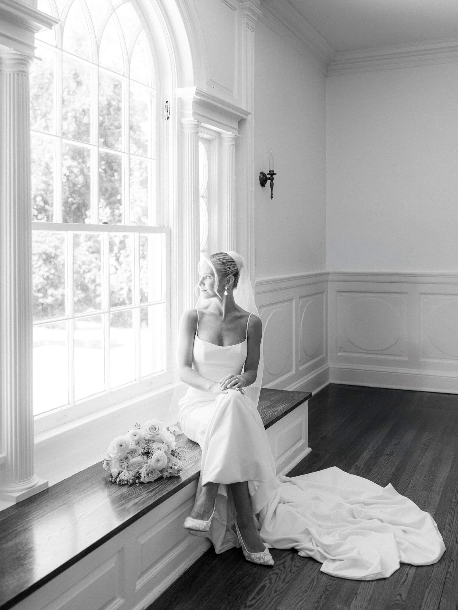 Black and white image of a bride sitting on the window seat with her bouquet next to her at a Rust Manor House wedding.